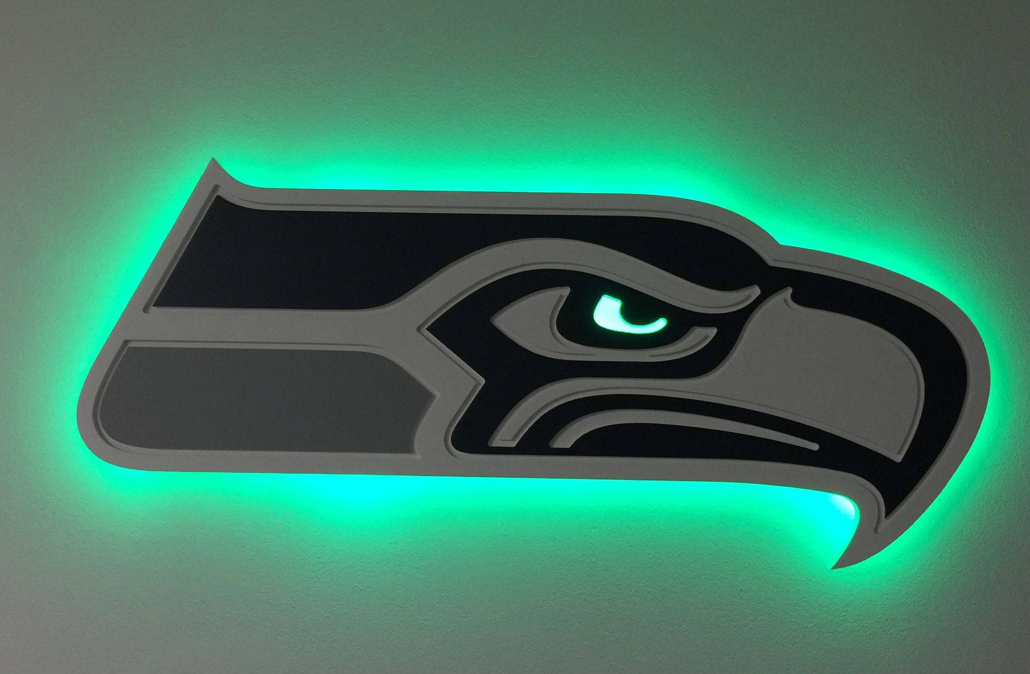 Seattle Seahawks 桌布 壁紙 — 一個發光的綠色西雅圖海鷹隊標誌牆燈，帶有兇猛的鷹眼，投射出充滿活力的霓虹光暈。