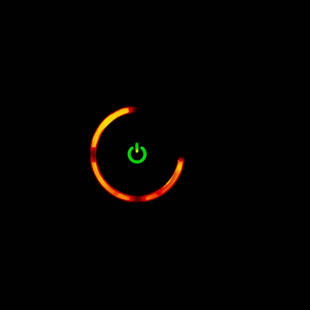Xbox 桌布 壁紙 — 一個發光的綠色電源符號，位於溫暖的橙色載入弧線中央，背景為黑色。