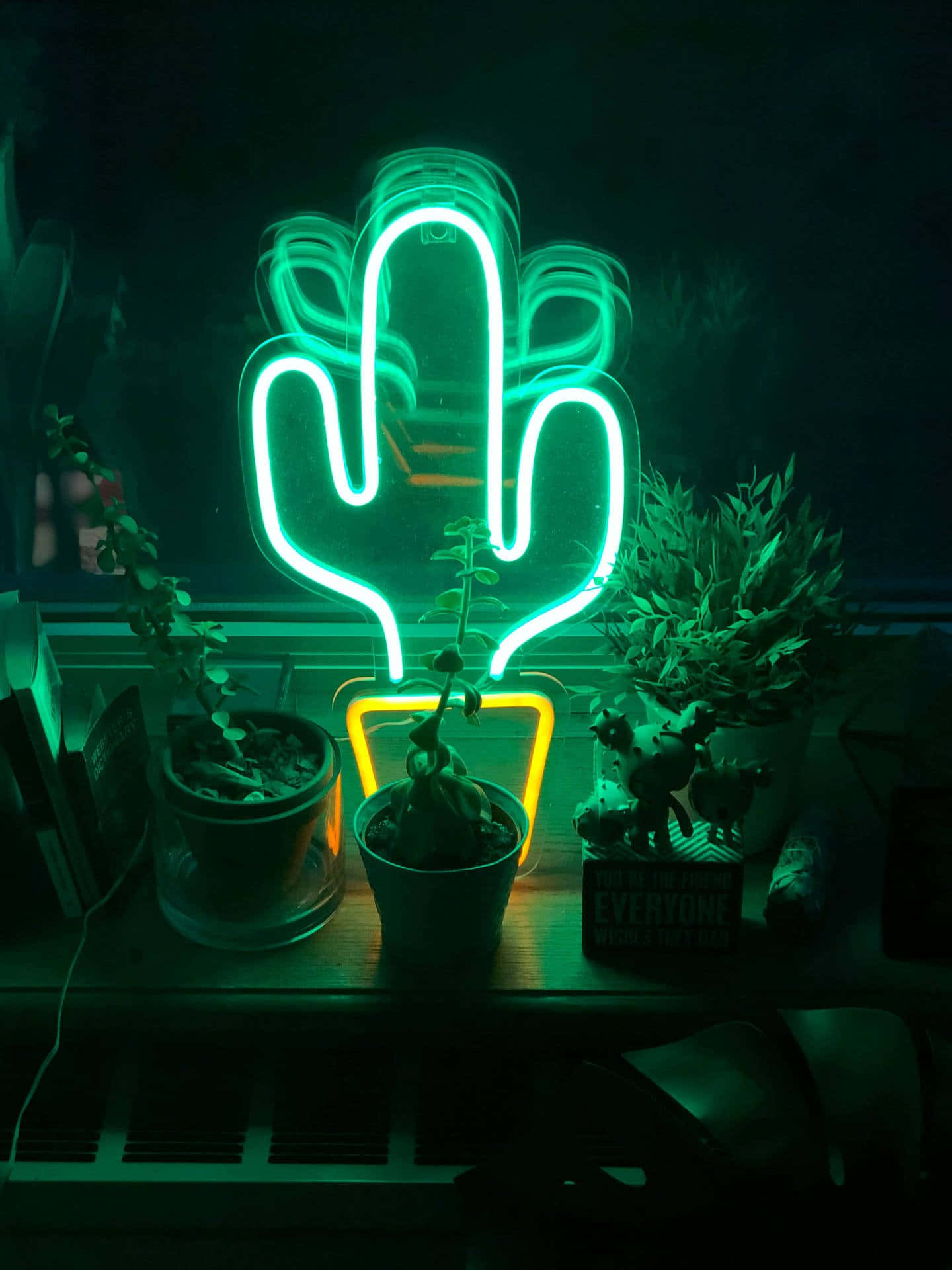 Neon Light 桌布 壁紙 — 一個發光的綠色霓虹仙人掌燈照亮了一個黑暗的架子，上面有盆栽植物和一個小雕像。