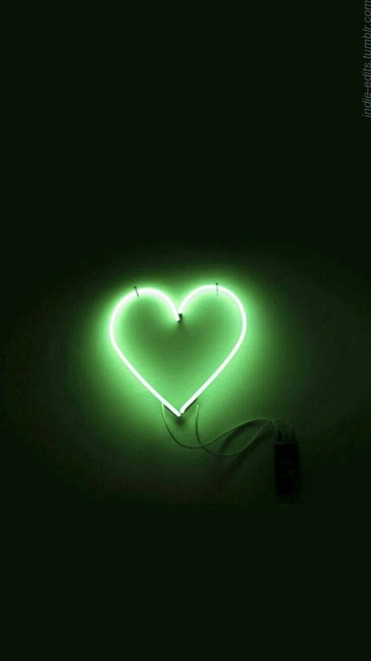 Green Heart 桌布 壁紙 — 一個發光的綠色霓虹心形標誌在簡約環境中，對著深色牆壁投射出柔和的光線。