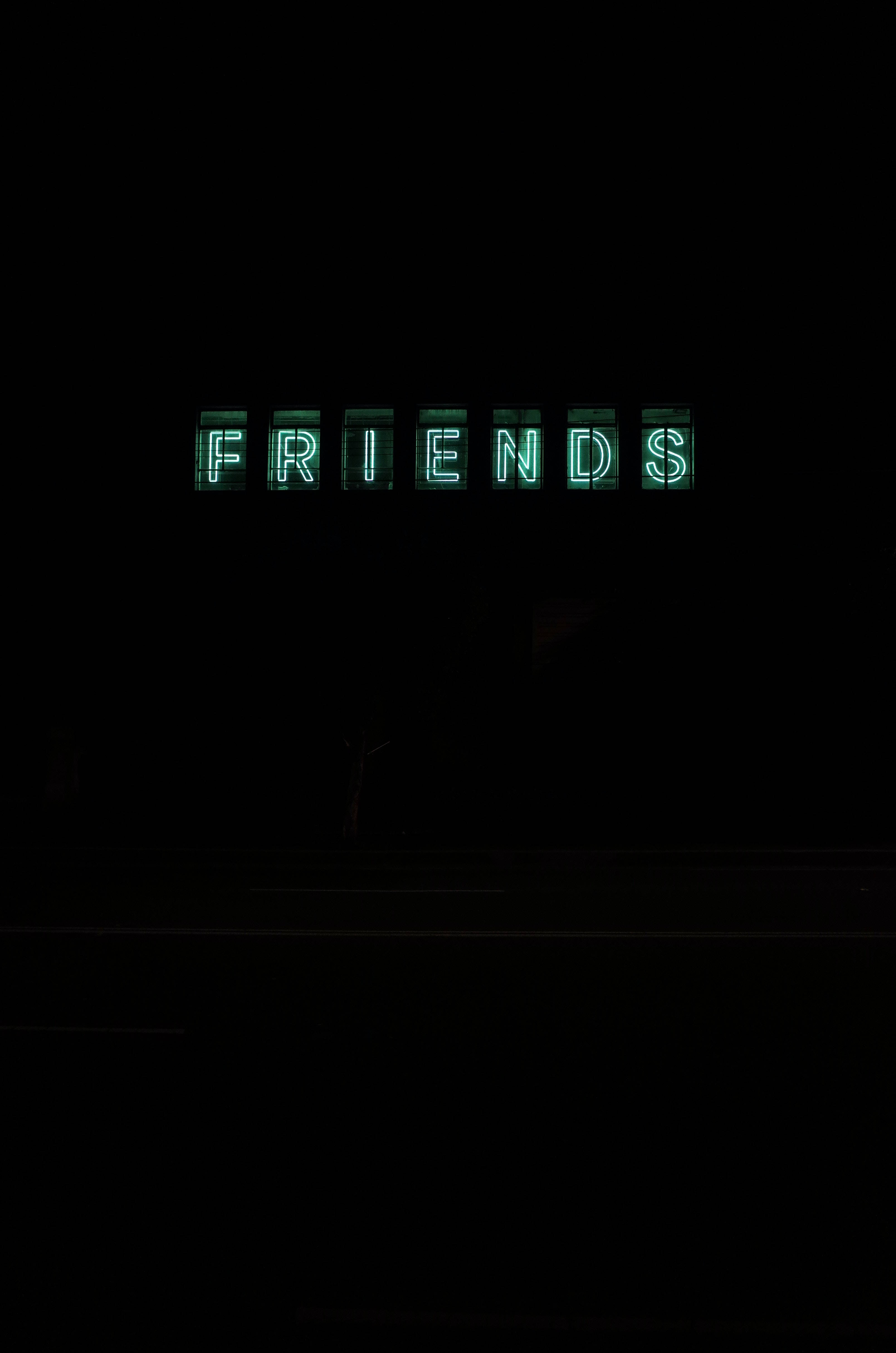 Screen 桌布 壁紙 — 一個發光的綠色霓虹燈牌，拼寫出 FRIENDS，在漆黑的夜空中格外突出。