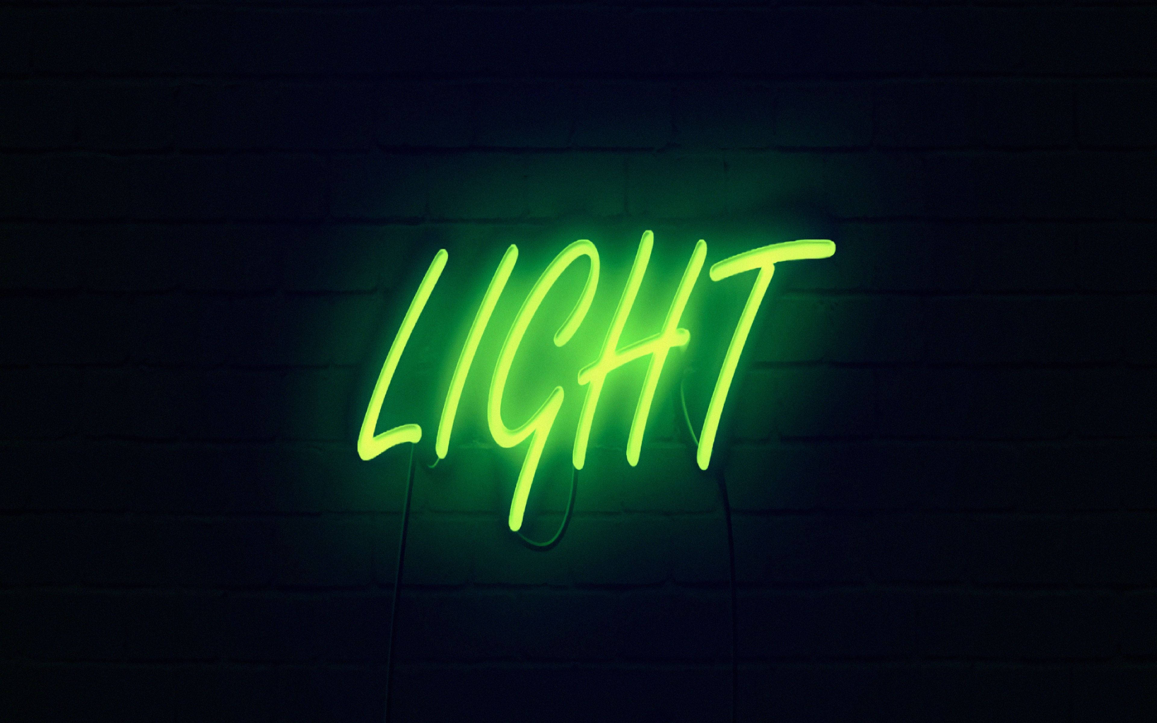 Neon Green Aesthetic 桌布 壁紙 — 一個發光的綠色霓虹燈牌，拼寫著 'LIGHT'，在昏暗的環境中對著深色磚牆投射出鮮豔的光芒。