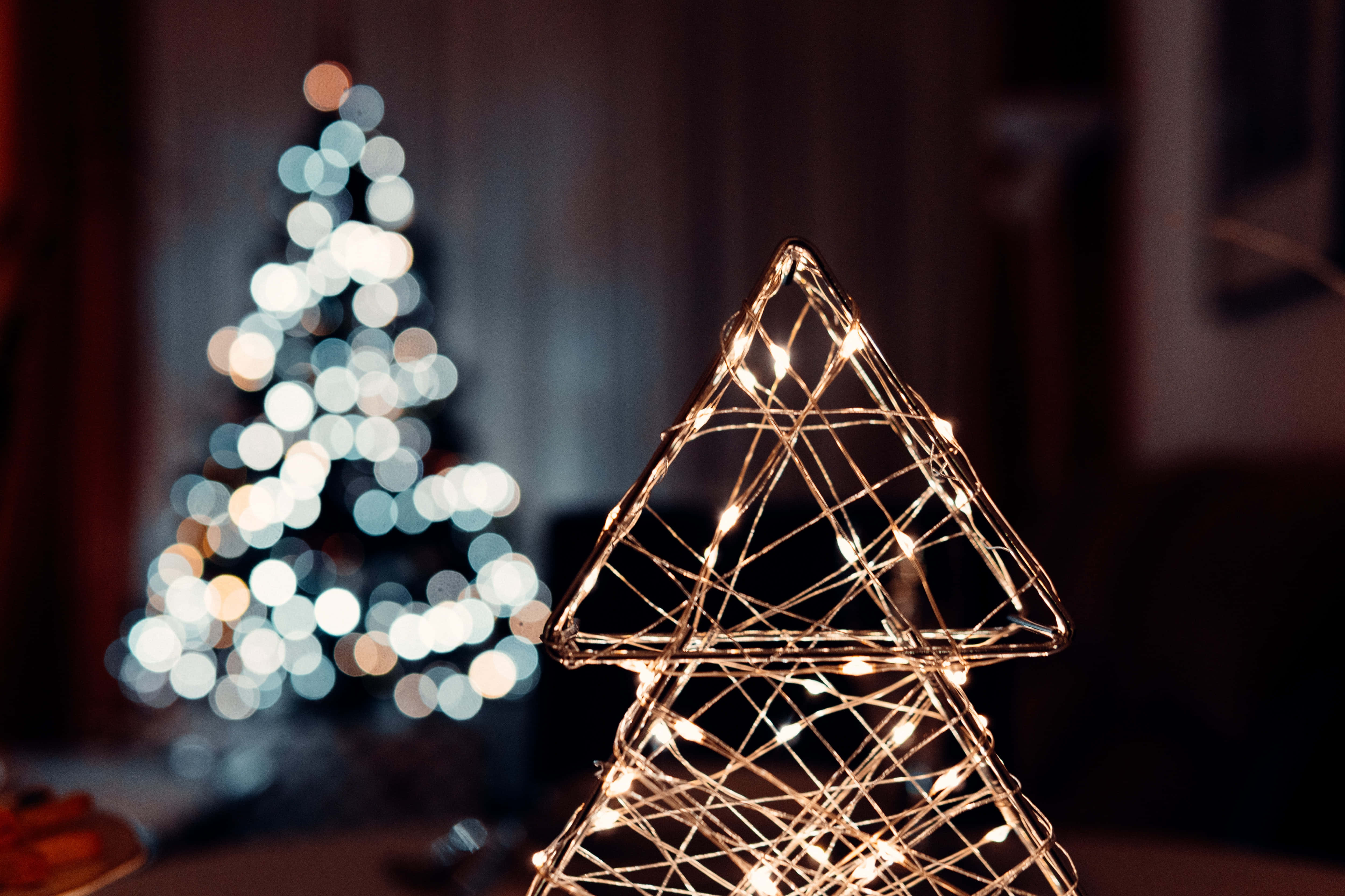 Christmas Light 桌布 壁紙 — 一個發光的線框聖誕樹，裝飾著溫暖的仙女燈，位於前景，後面有一個模糊的散景聖誕樹。