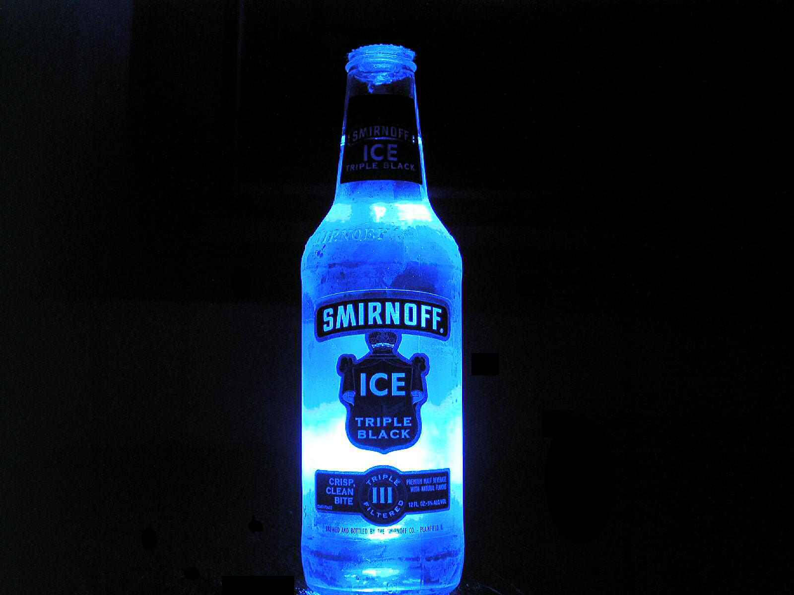 alcohol 桌布 壁紙 — 一個發光的藍色Smirnoff Ice Triple Black酒瓶，在漆黑背景中閃耀。