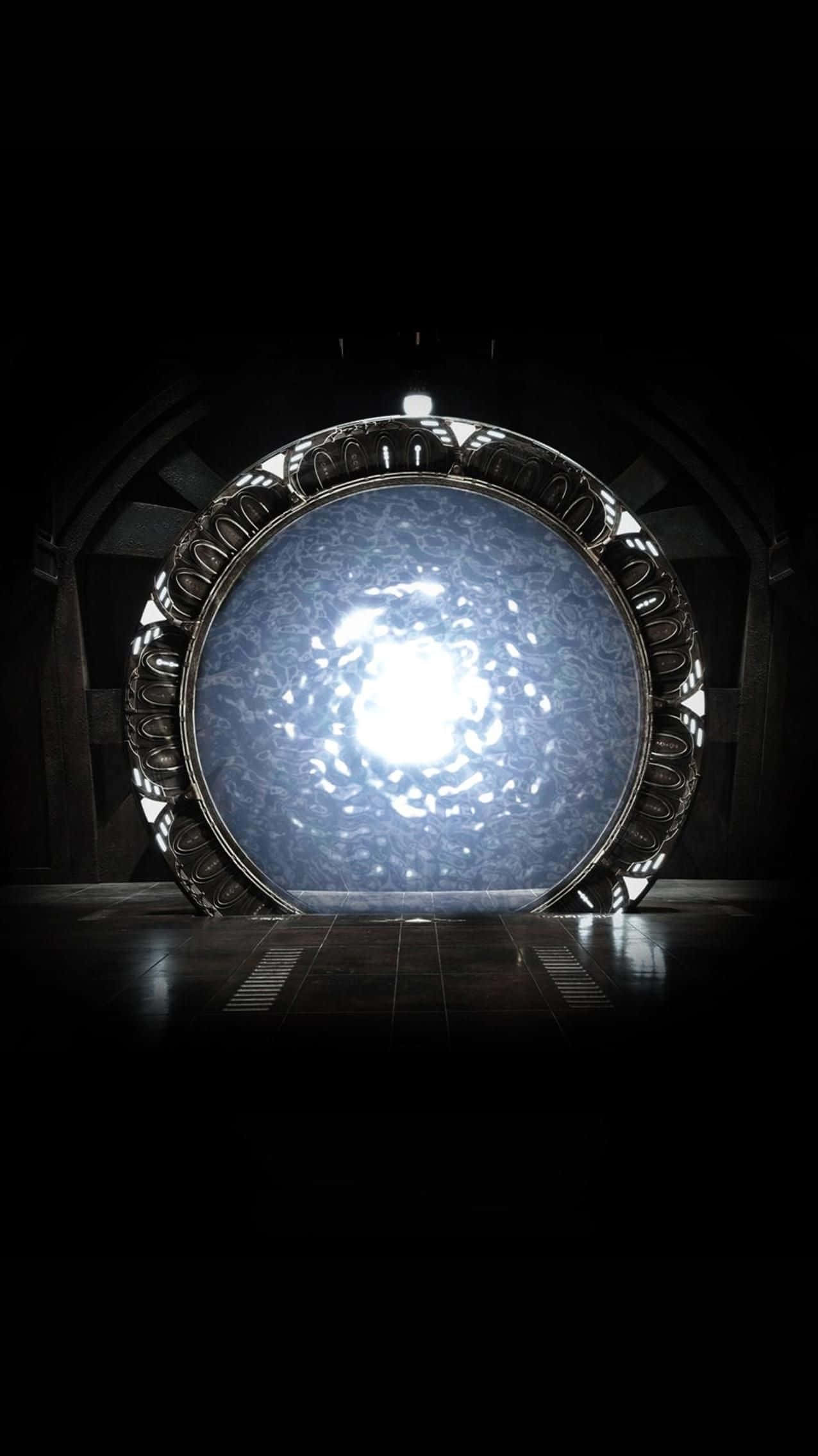 Stargate 桌布 壁紙 — 一個發光的藍色圓形傳送門，帶有複雜的金屬框架，在黑暗的石室中發出明亮的光芒。