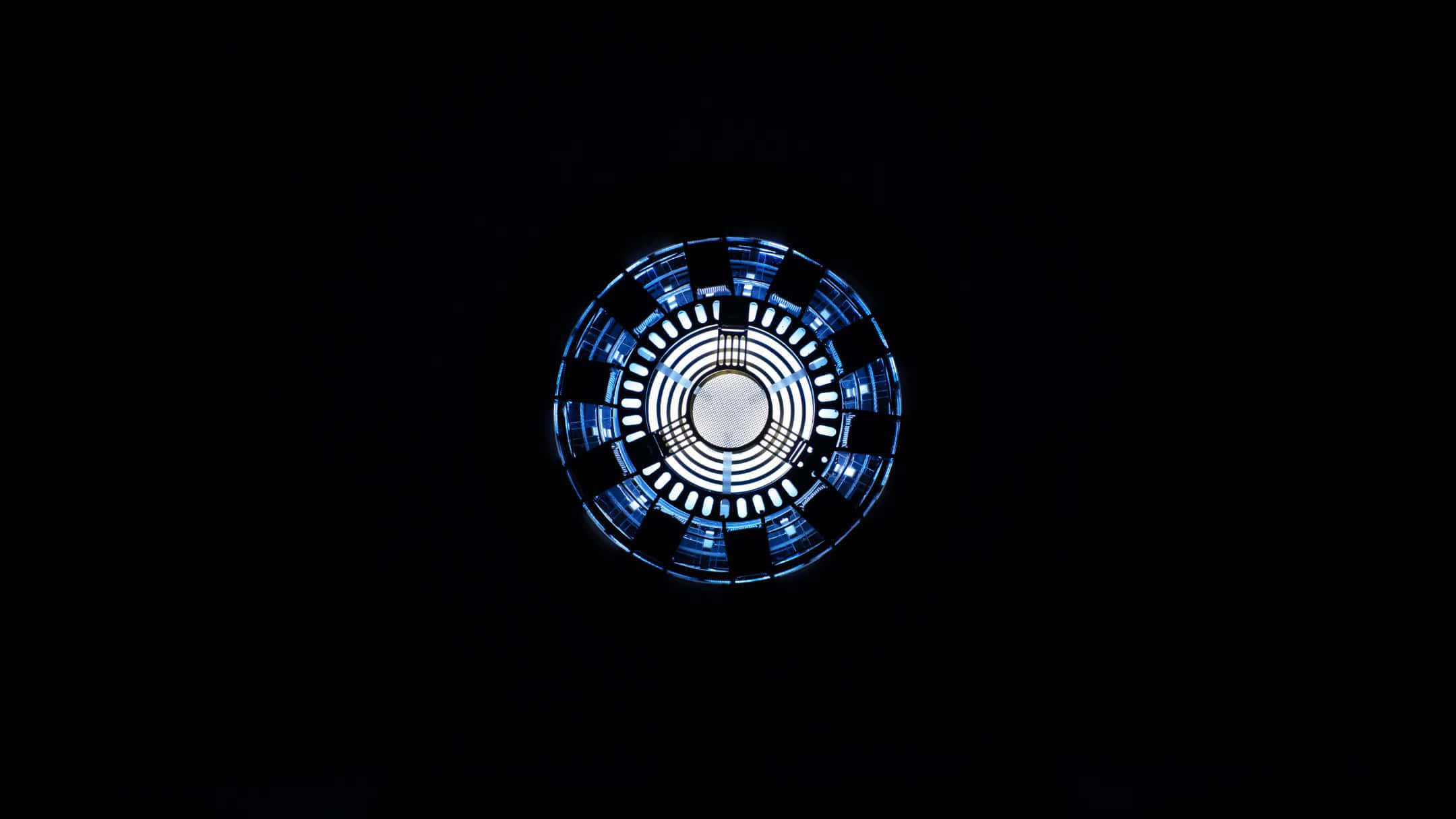 Best Marvel 桌布 壁紙 — 一個發光的藍色圓形電弧反應器在漆黑的背景下脈動著能量。