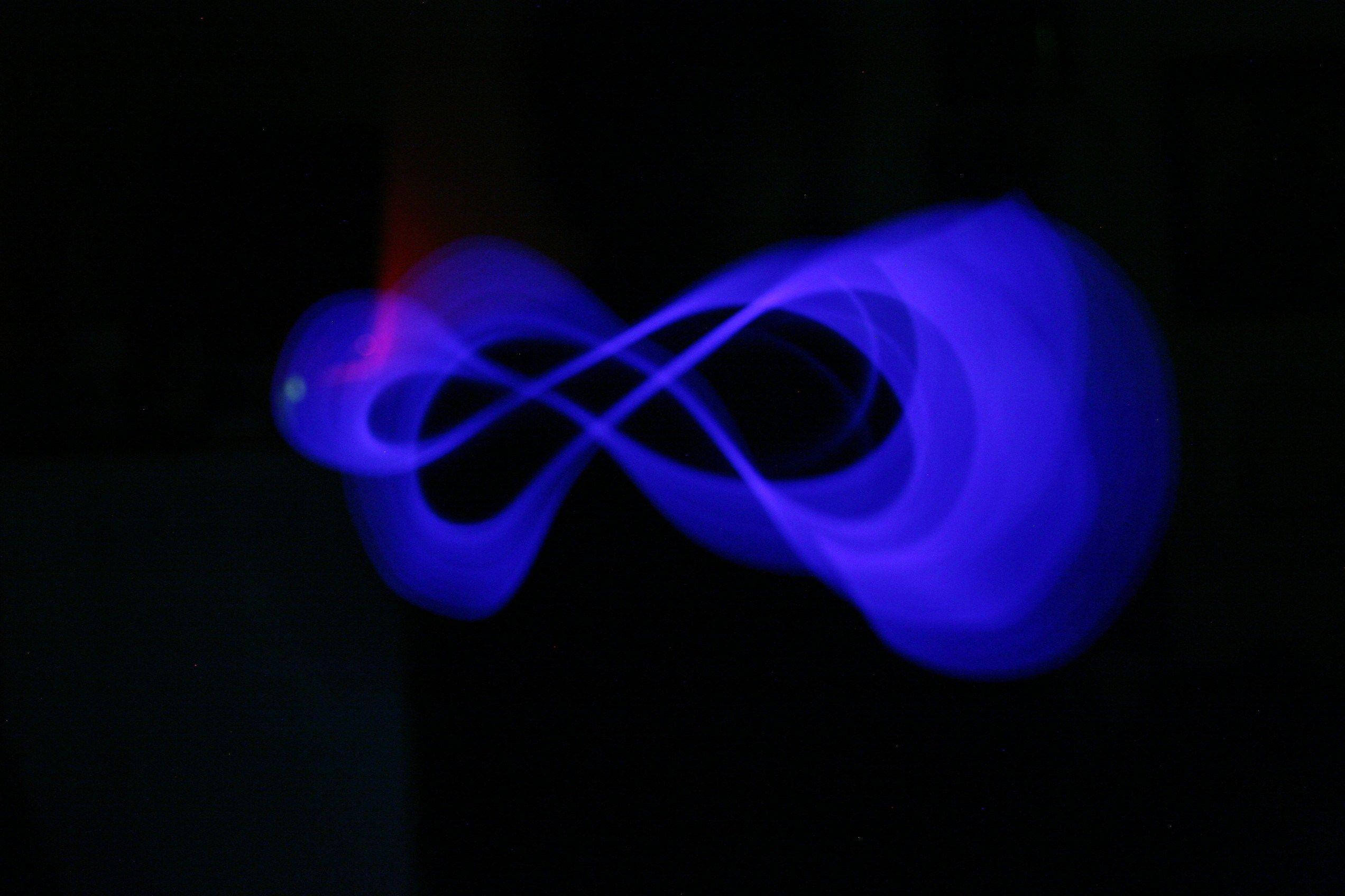 Infinity Symbol 桌布 壁紙 — 一個發光的藍色無限符號，帶有一絲紅色光跡，襯在漆黑的背景上。