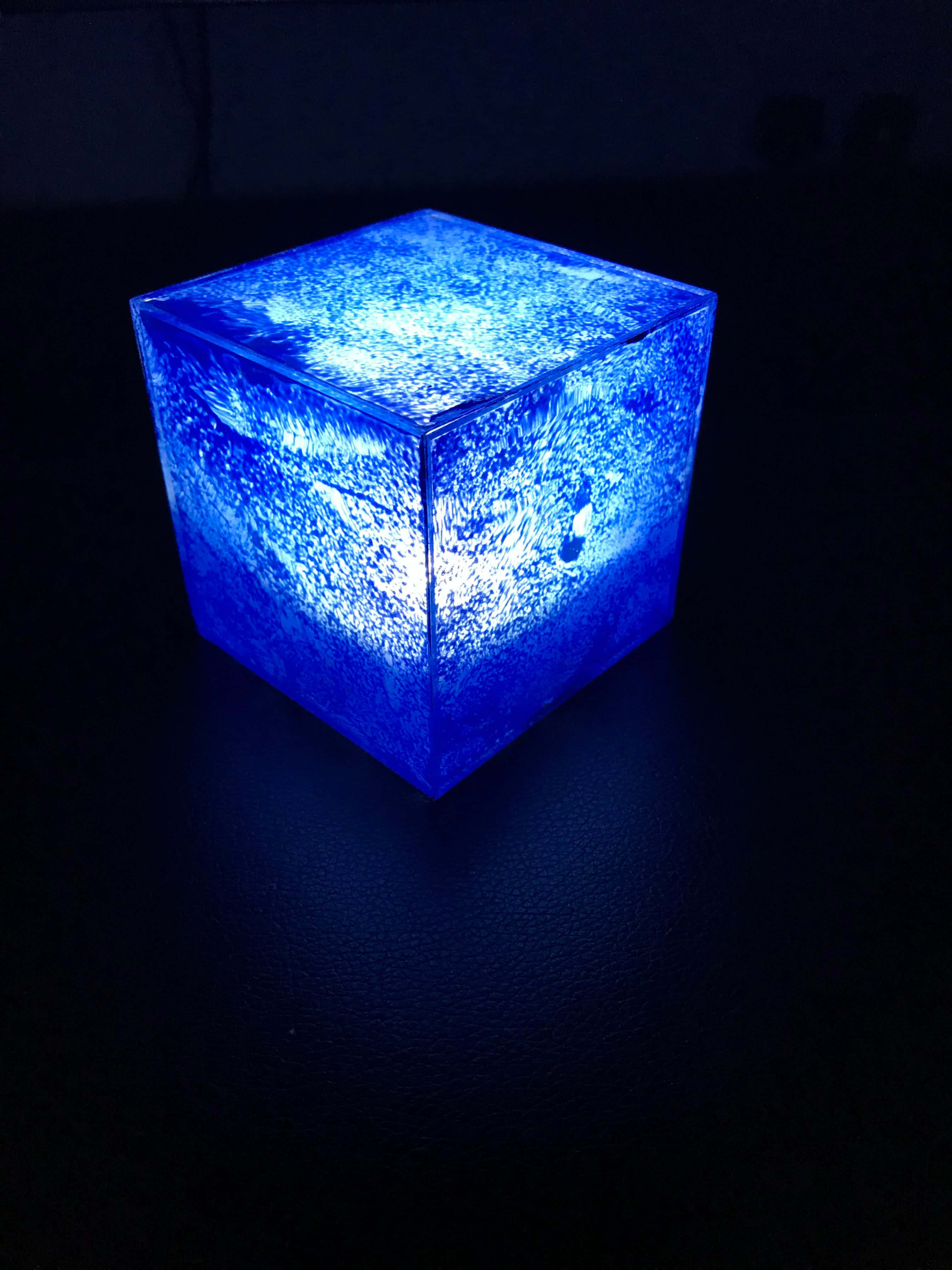 Space Stone 桌布 壁紙 — 一個發光的藍色立方體，表面帶有紋理，在黑暗背景下發出柔和的光線。