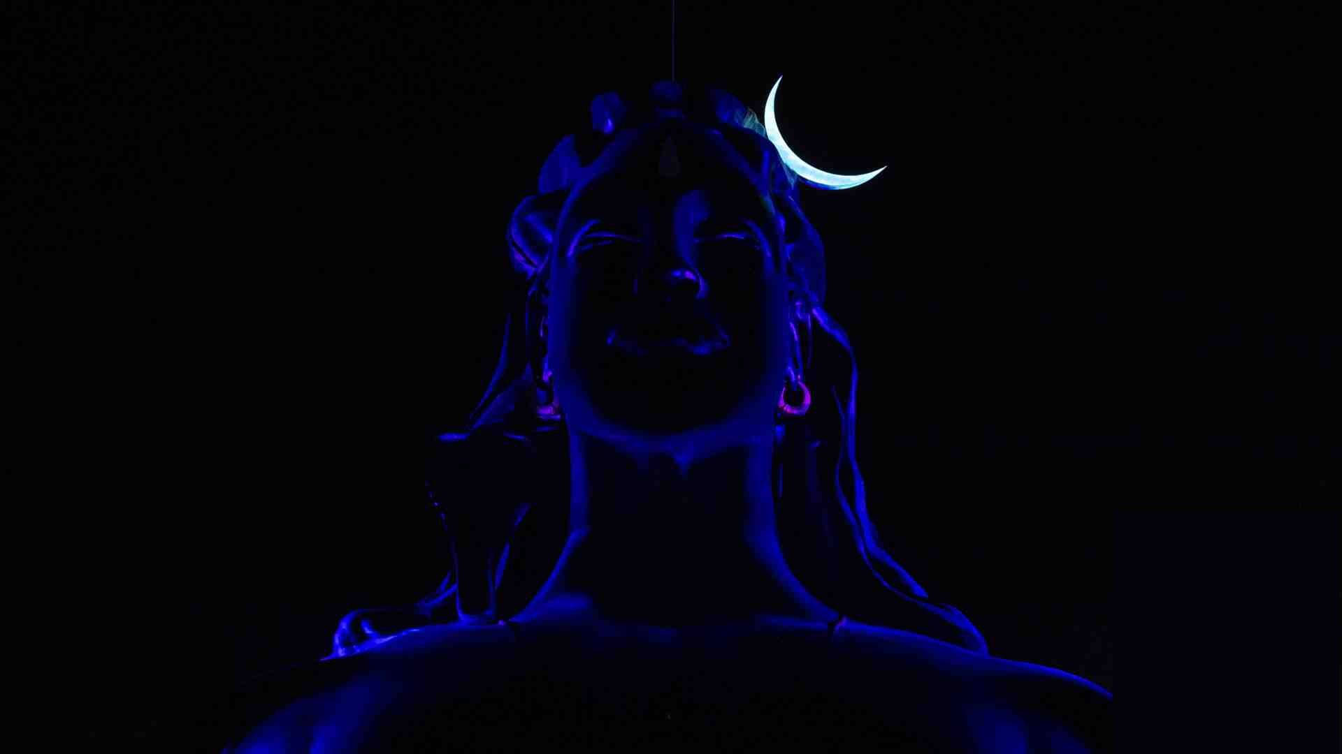 shiva dark 桌布 壁紙 — 一個發光的藍色雕像，描繪一位頭上有新月、神情安詳的神祇，背景為黑色。