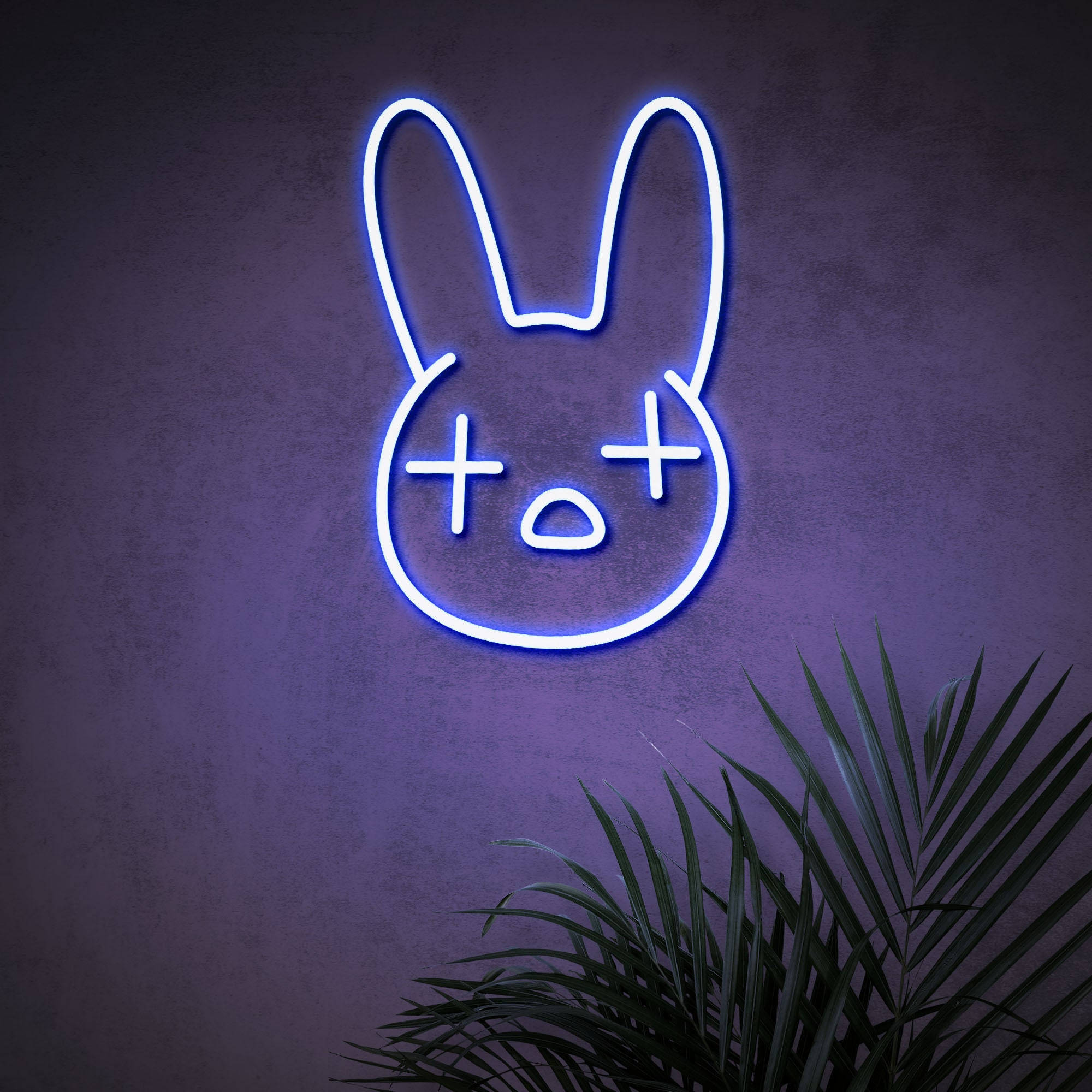 Bad Bunny Logo 桌布 壁紙 — 一個發光的藍色霓虹兔頭，帶有X形眼睛和O形嘴巴，安裝在紫色牆壁上，上方有綠色棕櫚葉。