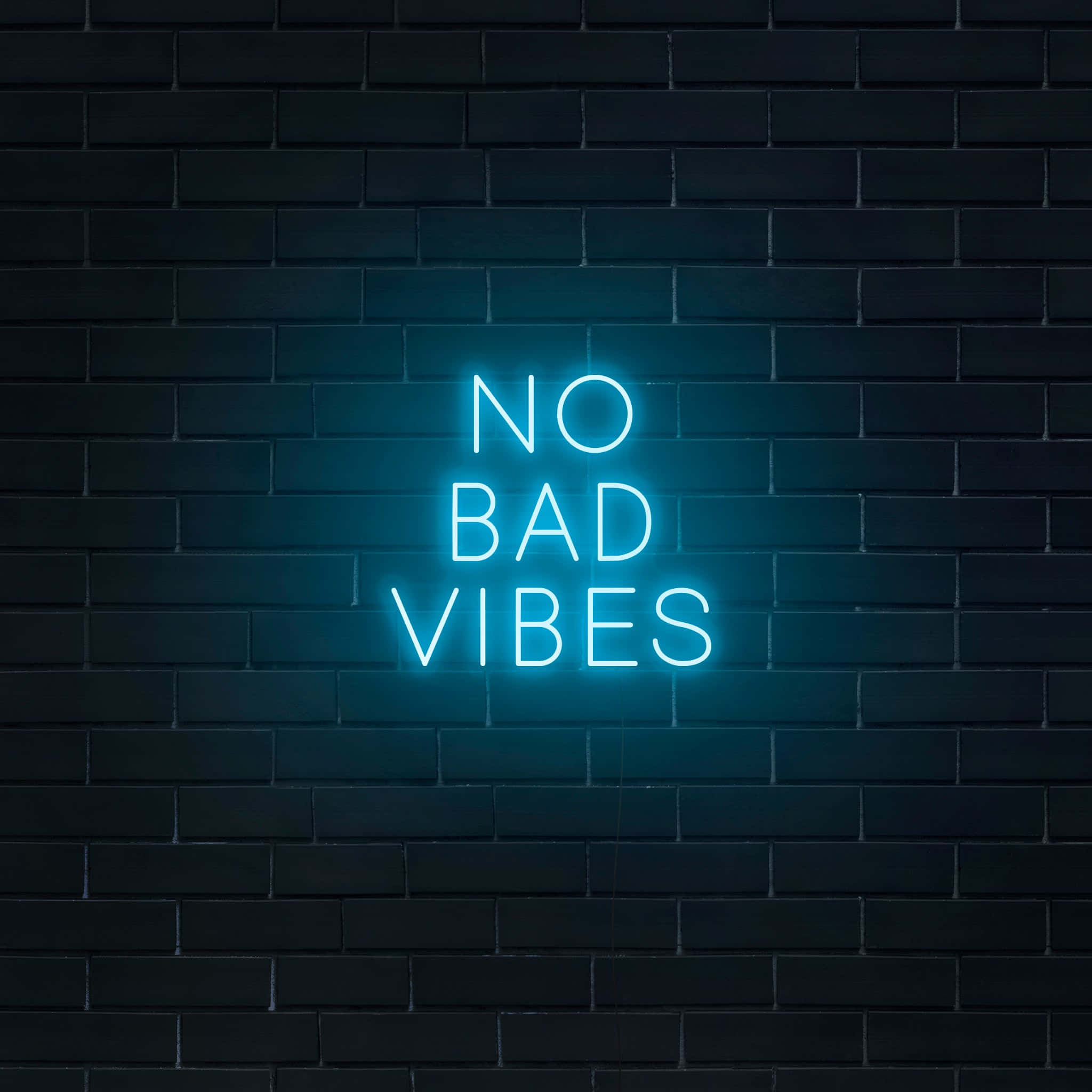 Bad Vibes 桌布 壁紙 — 一個發光的藍色霓虹燈牌，上面寫著 no bad vibes，夜晚安裝在深色磚牆上。