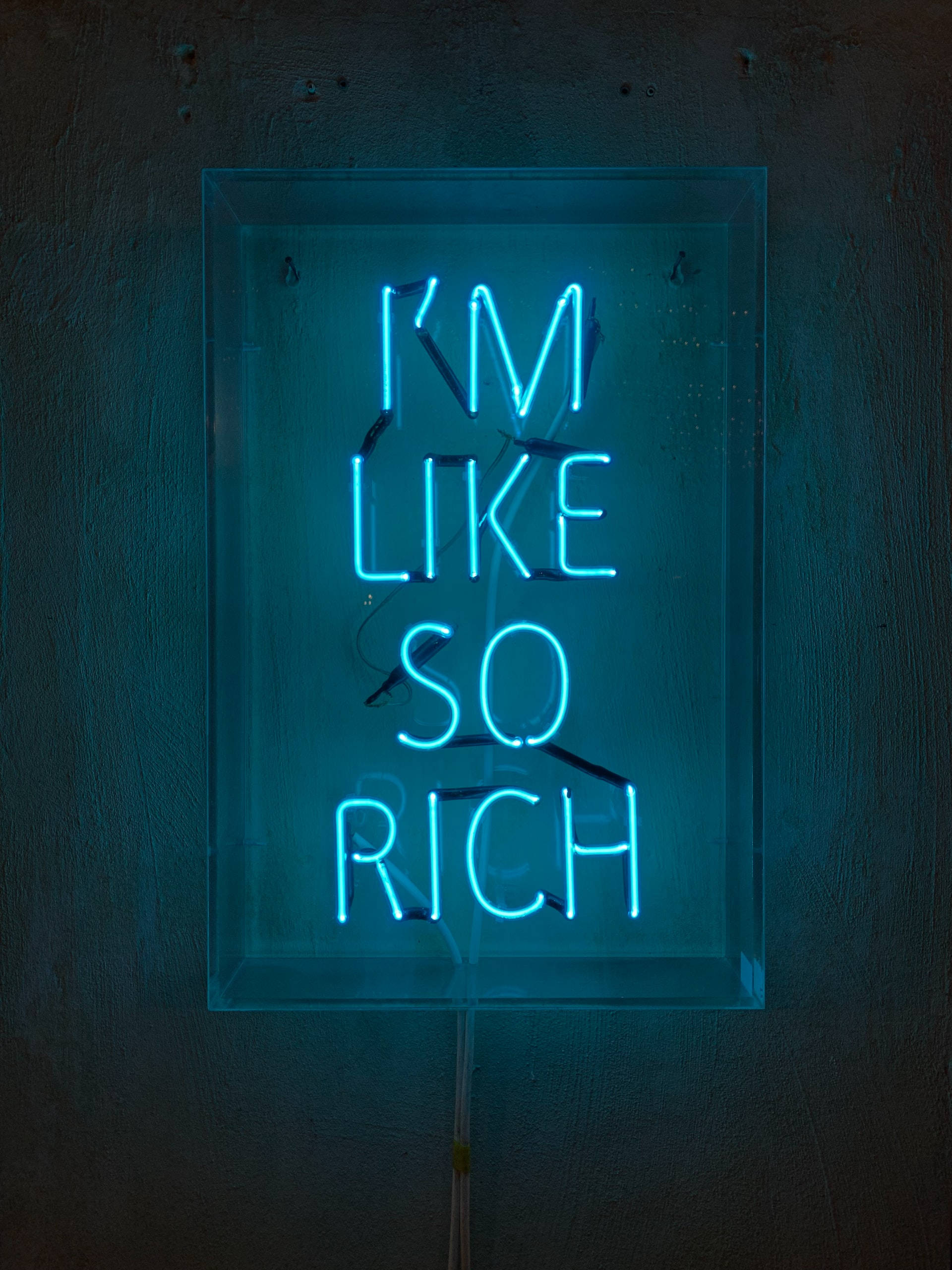 Neon Lights Aesthetic 桌布 壁紙 — 一個發光的藍色霓虹燈牌，上面寫著「I'M LIKE SO RICH」，裝在透明框架中，掛在深色紋理牆上。