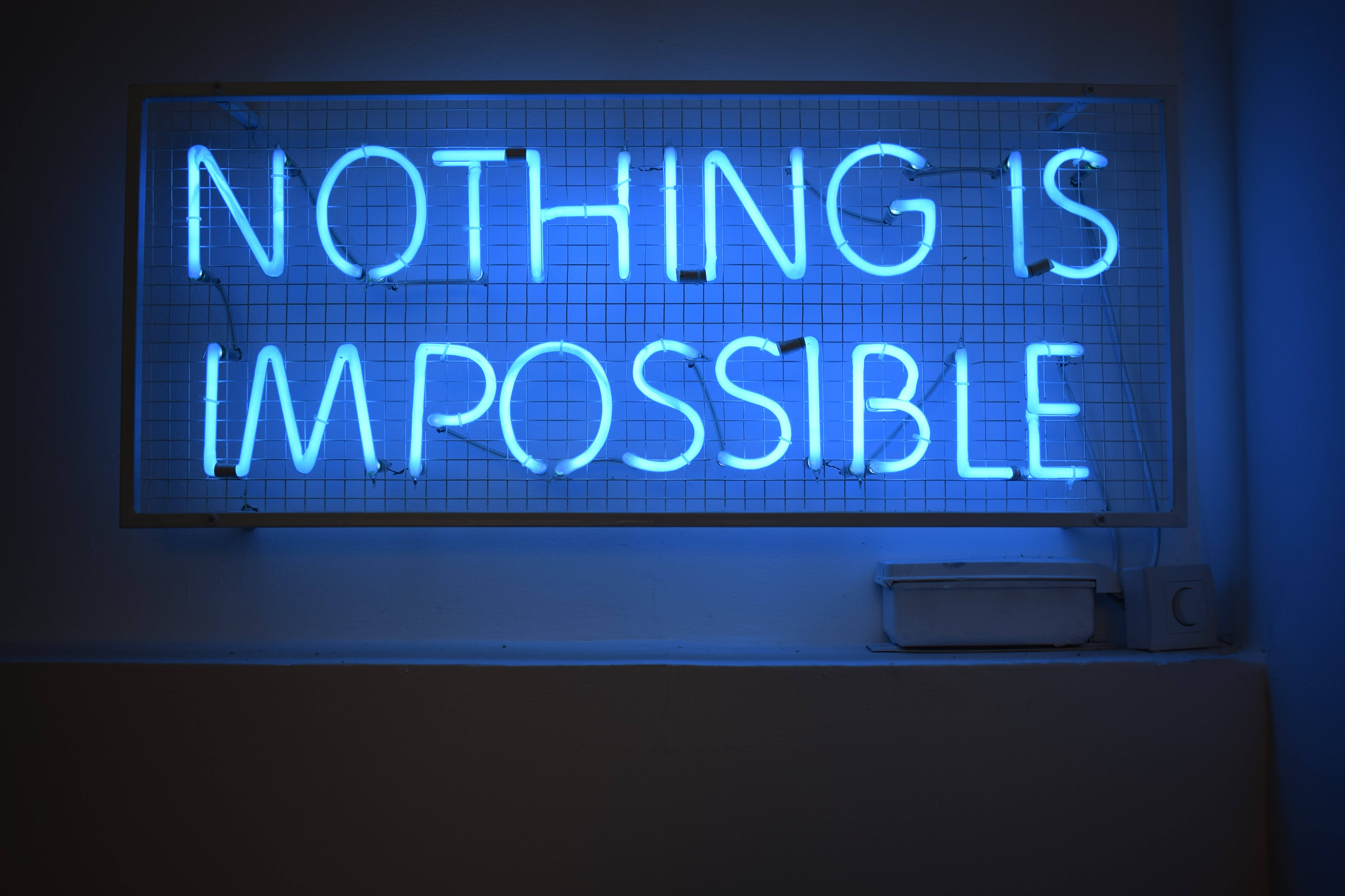 4K 霓虹 桌布 壁紙 — 一個發光的藍色霓虹燈牌，上面寫著 'NOTHING IS IMPOSSIBLE'，安裝在暗牆上的網格上。