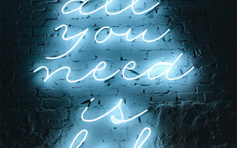 Aesthetic Tumblr Desktop 桌布 壁紙 — 一個發光的藍色霓虹燈牌，上面寫著「all you need is」，用柔和的光線照亮了深色紋理磚牆。