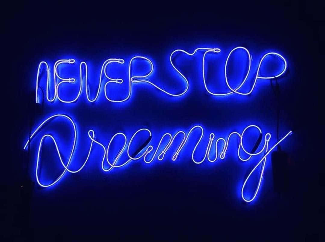 霓虹藍美學 桌布 壁紙 — 一個發光的藍色霓虹燈牌，上面寫著「NEVER STOP Dreaming」，背景為深色。