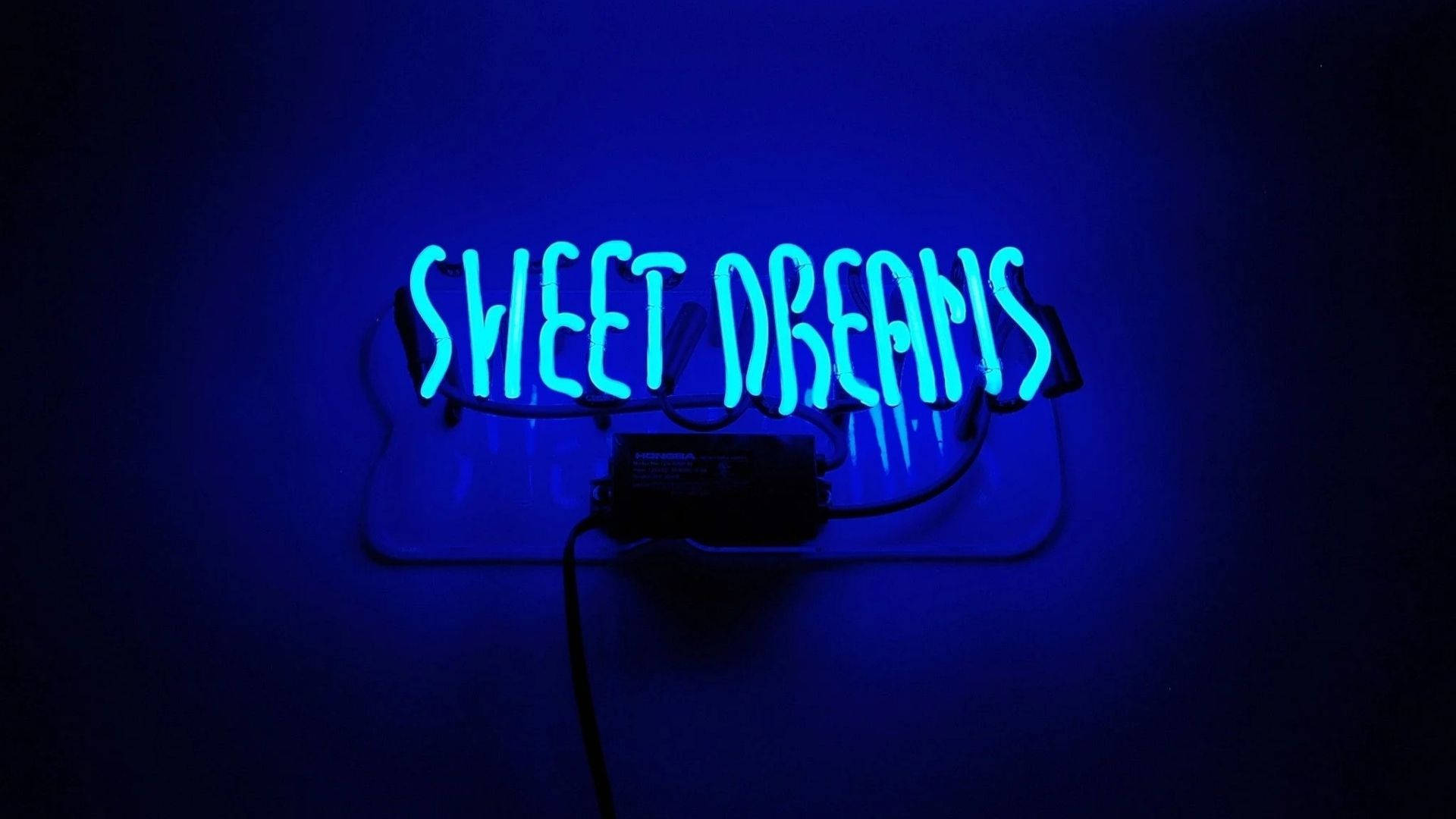 dreams 桌布 壁紙 — 一個發光的藍色霓虹燈牌，上面寫著 sweet dreams，在昏暗的房間中將柔和的光線投射在深色牆壁上。