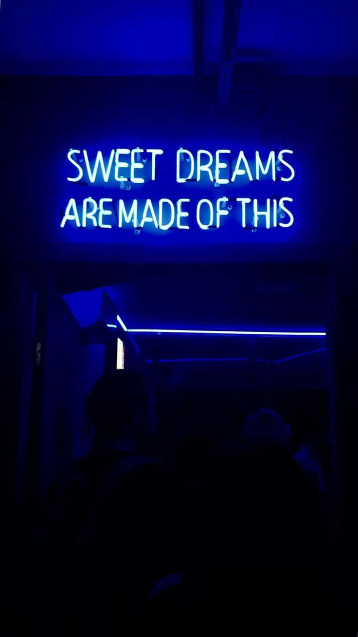 霓虹藍美學 桌布 壁紙 — 一個發光的藍色霓虹燈牌寫著 sweet dreams are made of this，在一個黑暗的房間裡，下方有剪影人物。