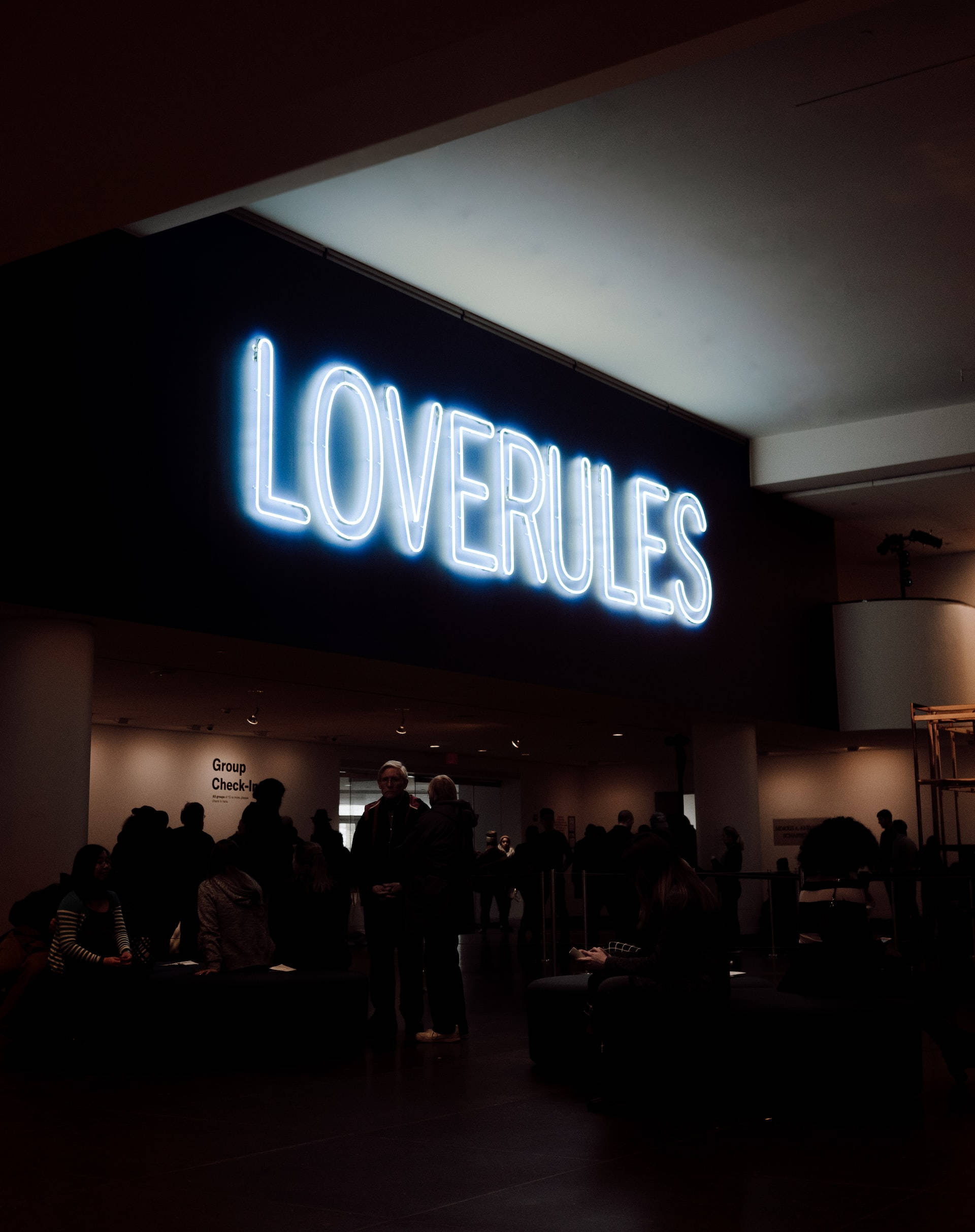 人物 桌布 壁紙 — 一個發光的藍色霓虹燈牌寫著LOVERULES，照亮了一個燈光昏暗的室內空間，下方有人影。