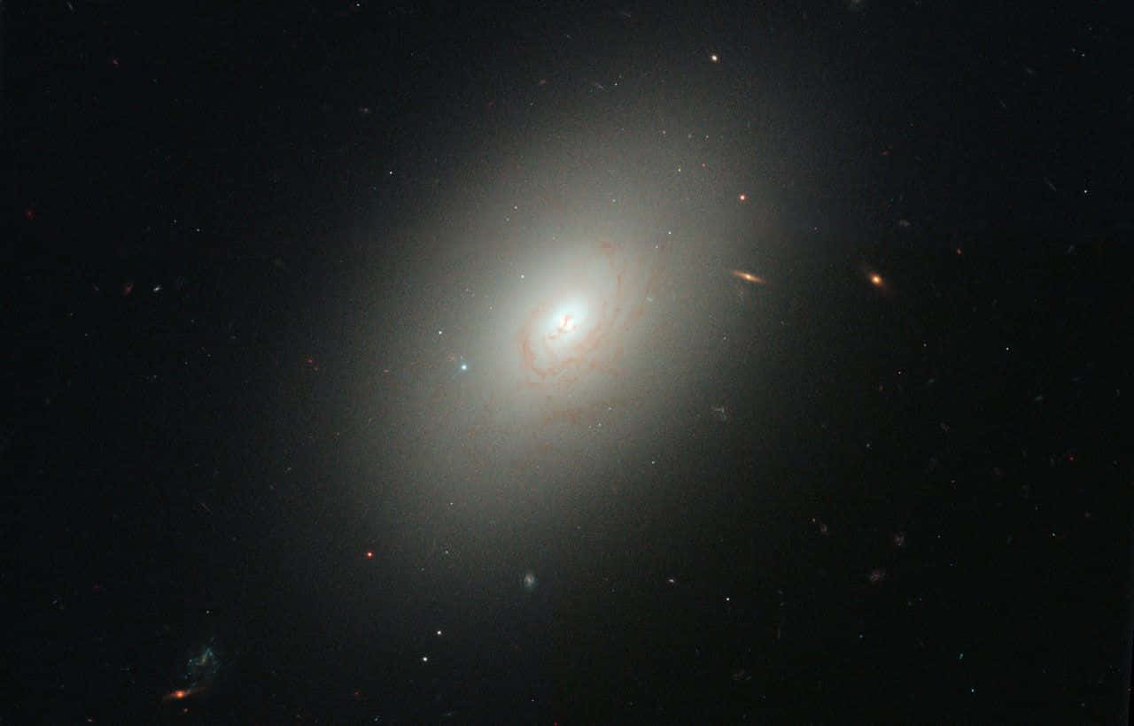 Elliptical Galaxy 桌布 壁紙 — 一個發光的螺旋星系，帶有旋轉的旋臂和明亮的核心，主宰著一個充滿恆星的宇宙虛空。