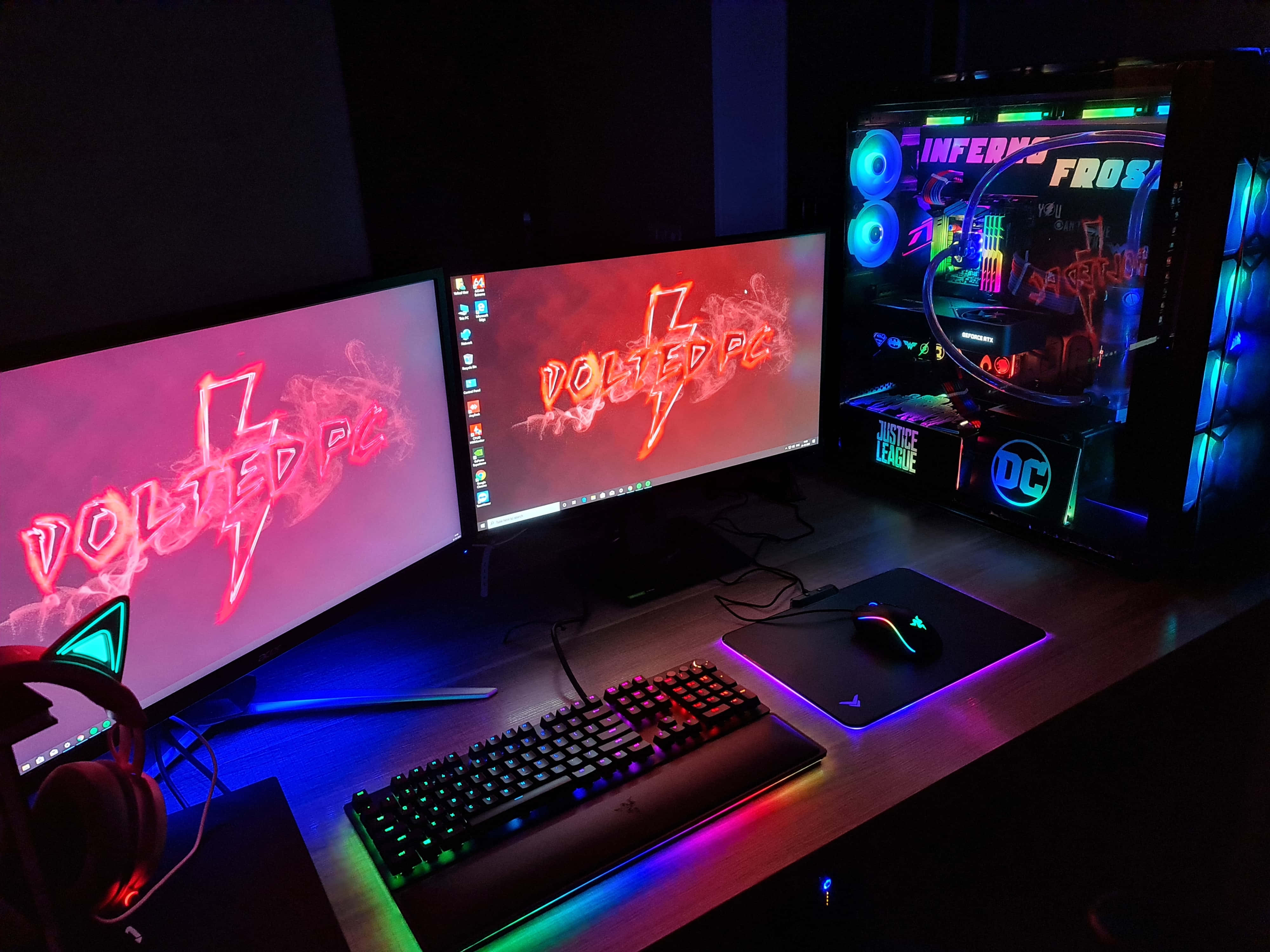 Gaming Pc Setup 桌布 壁紙 — 一個發光的遊戲設置，配備雙顯示器顯示霓虹燈「VoltED PC」標誌，以及一個用藍色和紫色LED燈照亮的自訂PC機箱。
