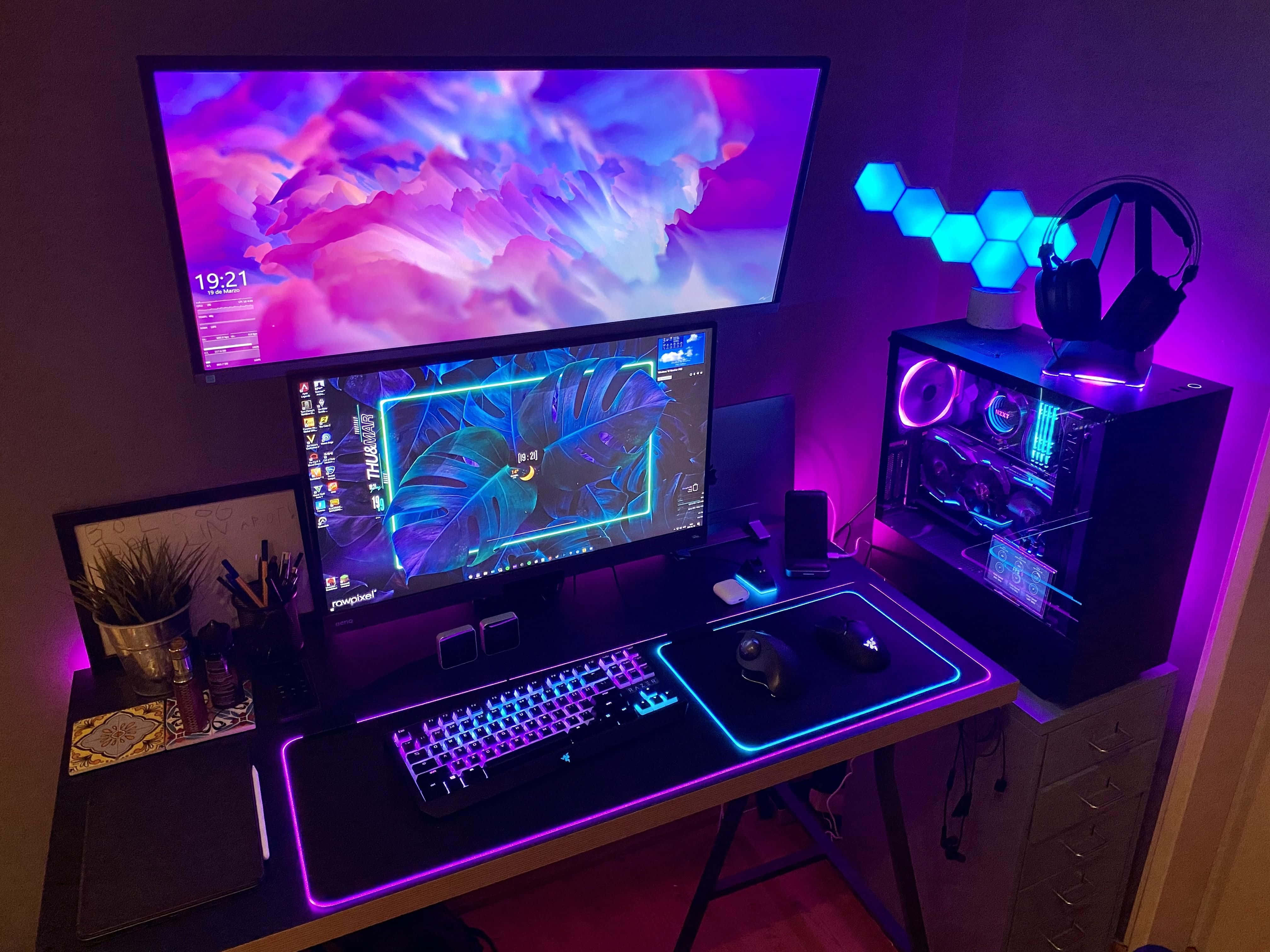 Gaming Pc Setup 桌布 壁紙 — 一個發光的遊戲設置，配備雙顯示器、充滿活力的紫色和藍色LED燈光、自訂電腦及周邊設備，置於時尚的桌子上。