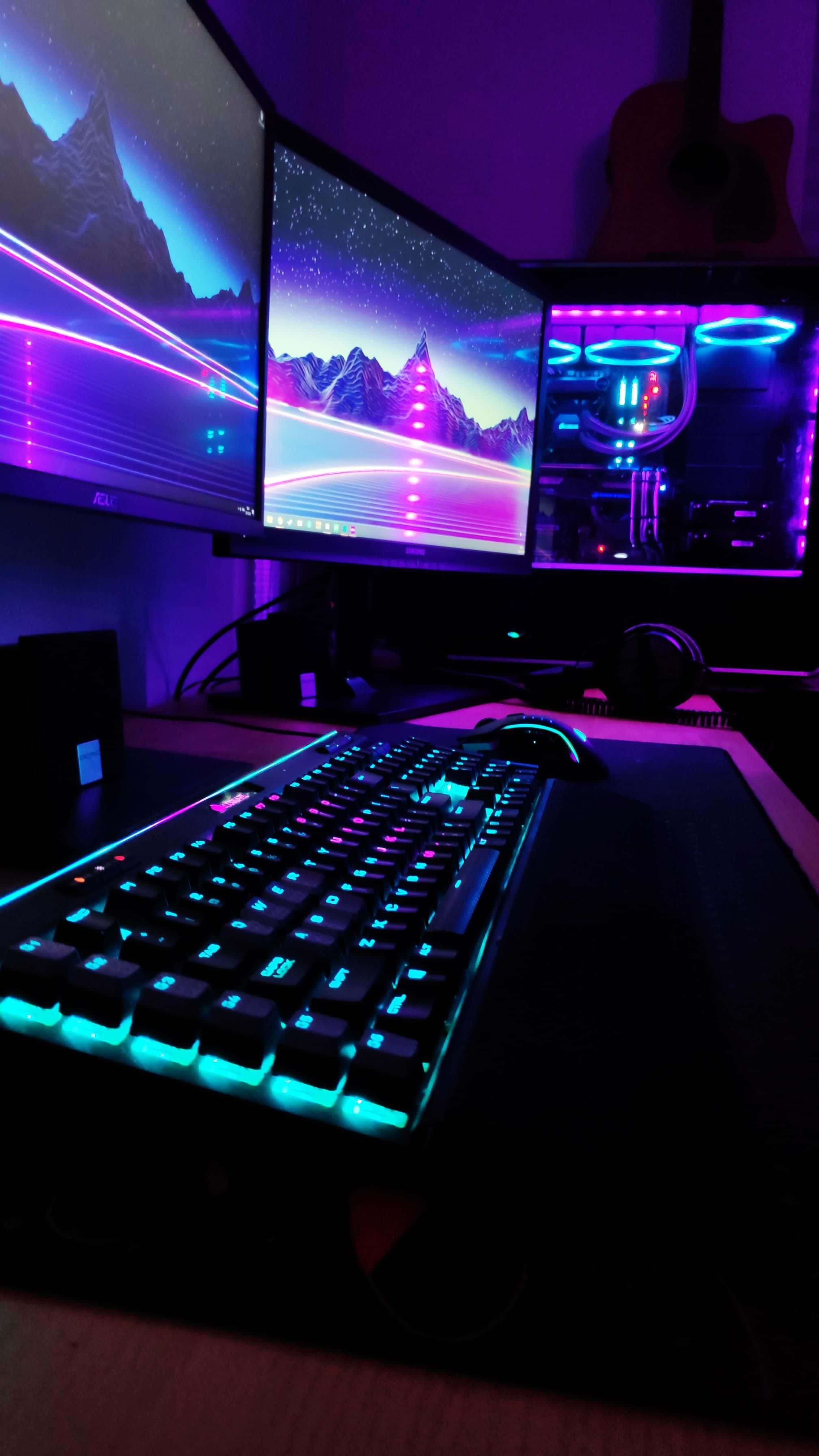 Gaming Accessories 桌布 壁紙 — 一個發光的遊戲設置，配有三個顯示器顯示霓虹山景，以及在紫色環境光下發光的RGB鍵盤。