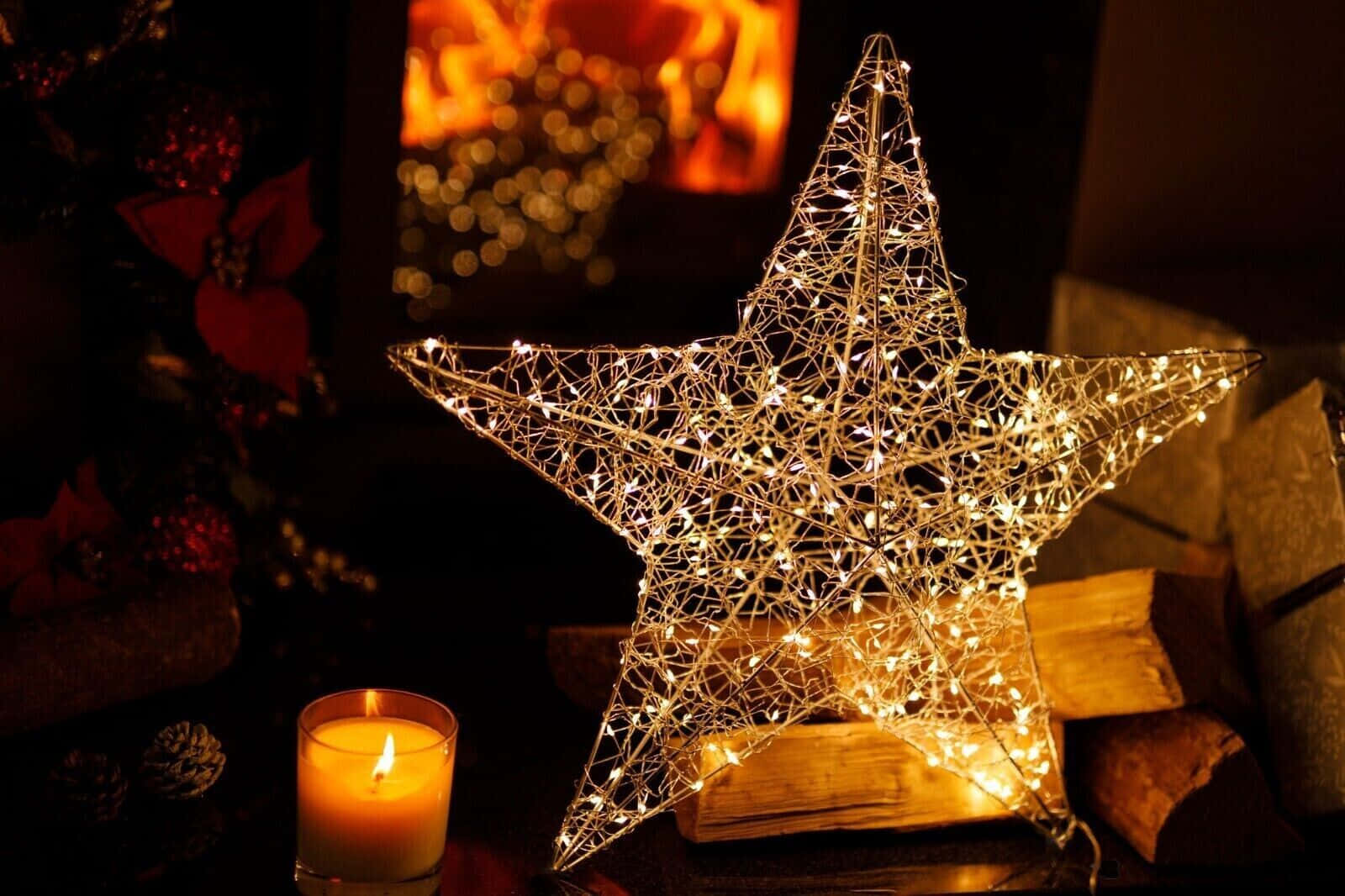 Christmas Star 桌布 壁紙 — 一個發光的金屬絲星星，飾有童話燈，放在蠟燭和壁爐旁邊，營造出舒適的節日氛圍。