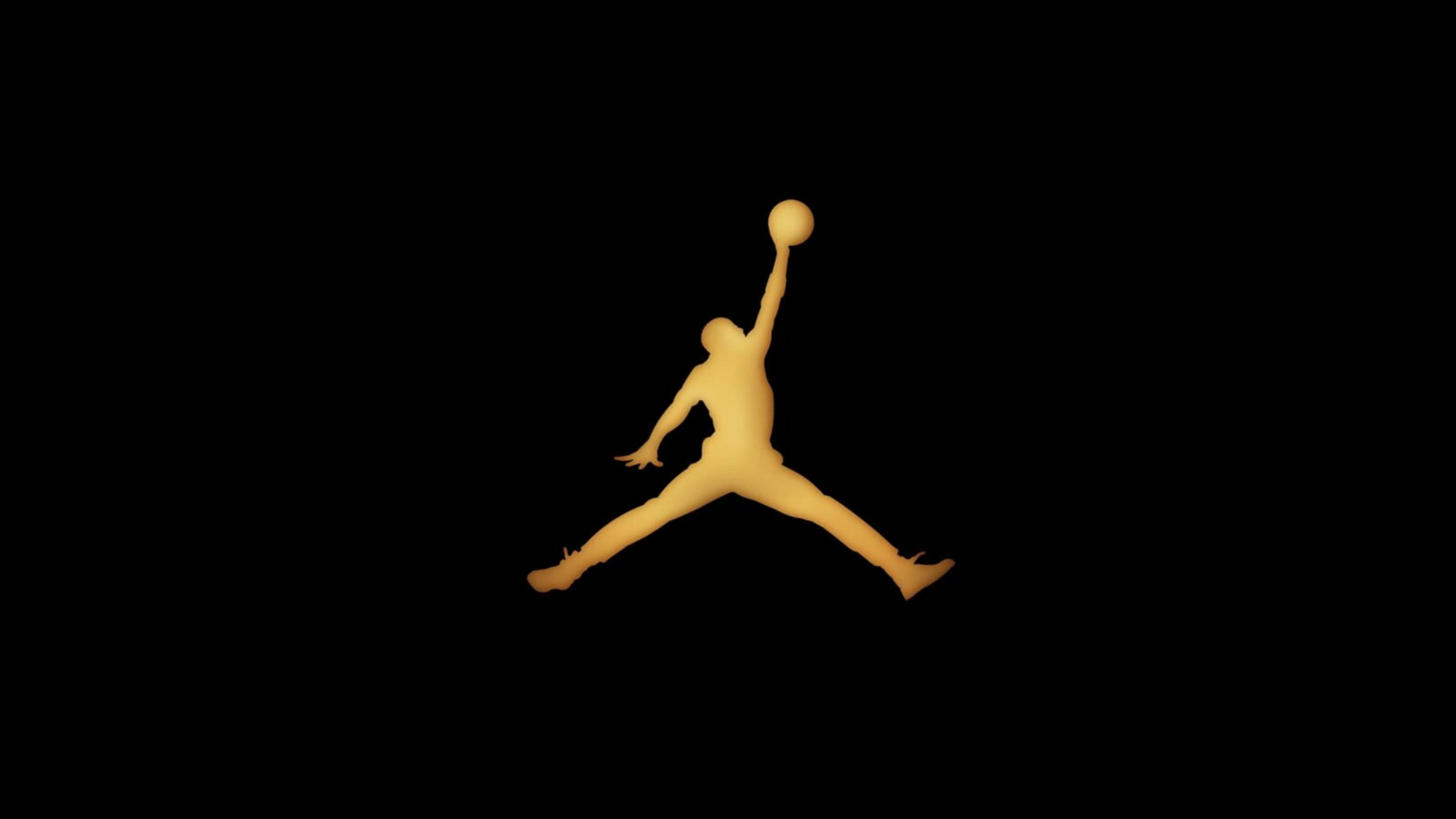 Air Jordan 桌布 壁紙 — 一個發光的金色剪影，描繪一名籃球運動員在半空中灌籃，背景為純黑色。