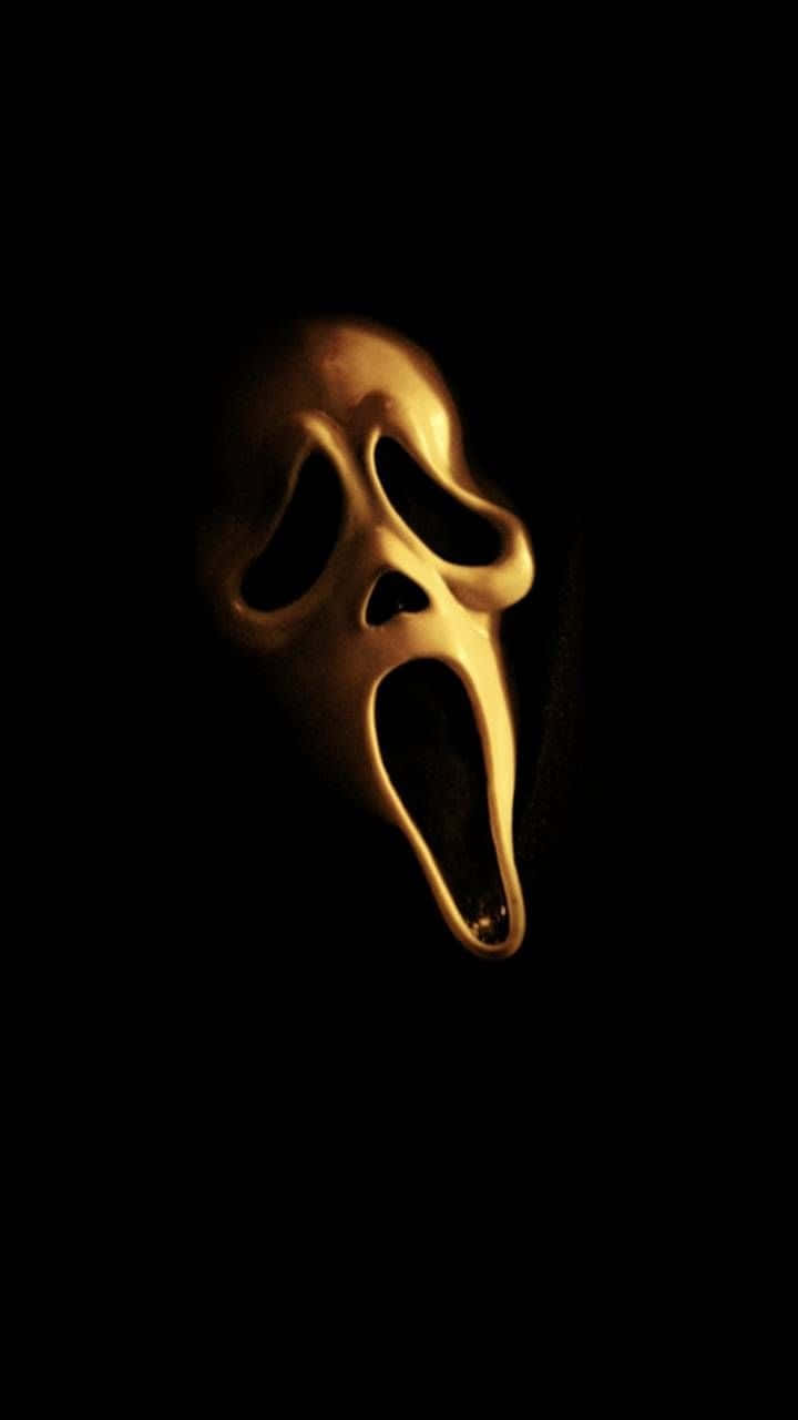 Scream Ghostface 桌布 壁紙 — 一個發光的金色驚聲尖叫面具漂浮在絕對的黑暗中，以其標誌性的恐怖設計投下詭異的陰影。