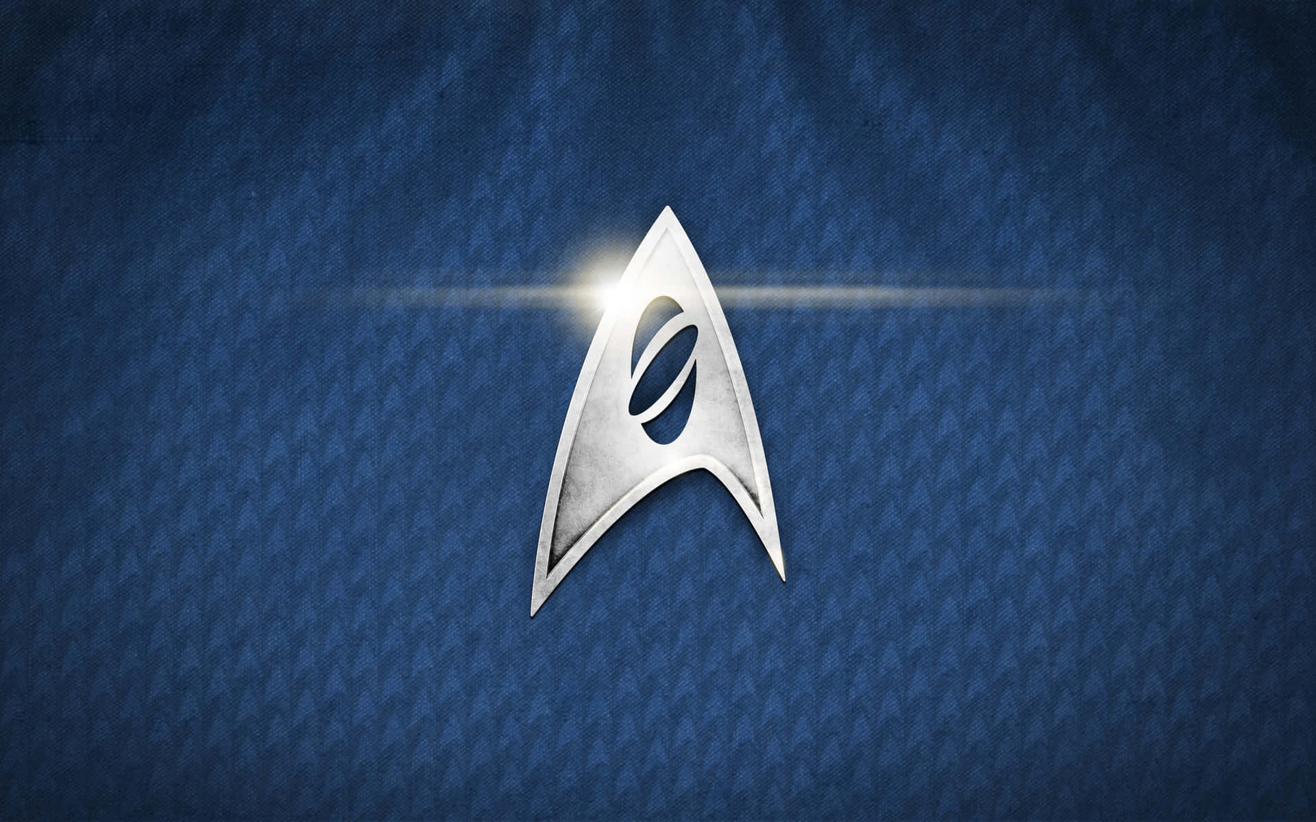 Starship 桌布 壁紙 — 一個發光的銀色星際艦隊徽章，居中在帶有紋理的藍色布料背景上，並有明亮的鏡頭光暈。