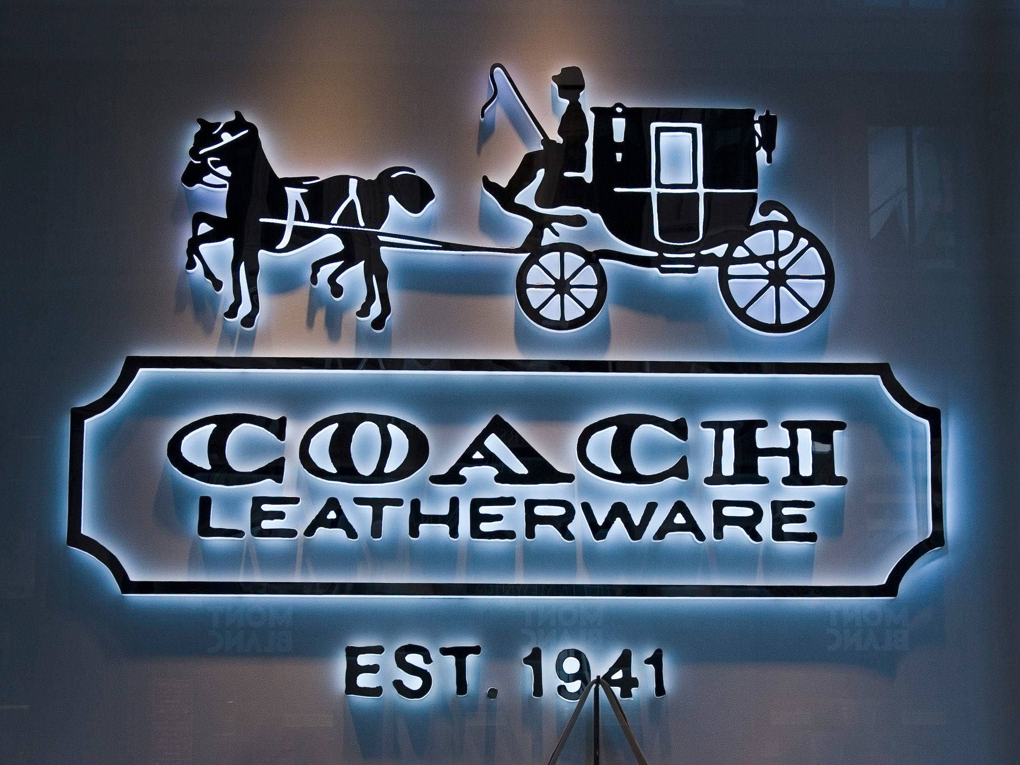 Coach 桌布 壁紙 — 一個發光的霓虹招牌展示一匹馬拉著馬車的黑色剪影，上方是粗體文字「COACH LEATHERWARE」，下方是「EST. 1941」。