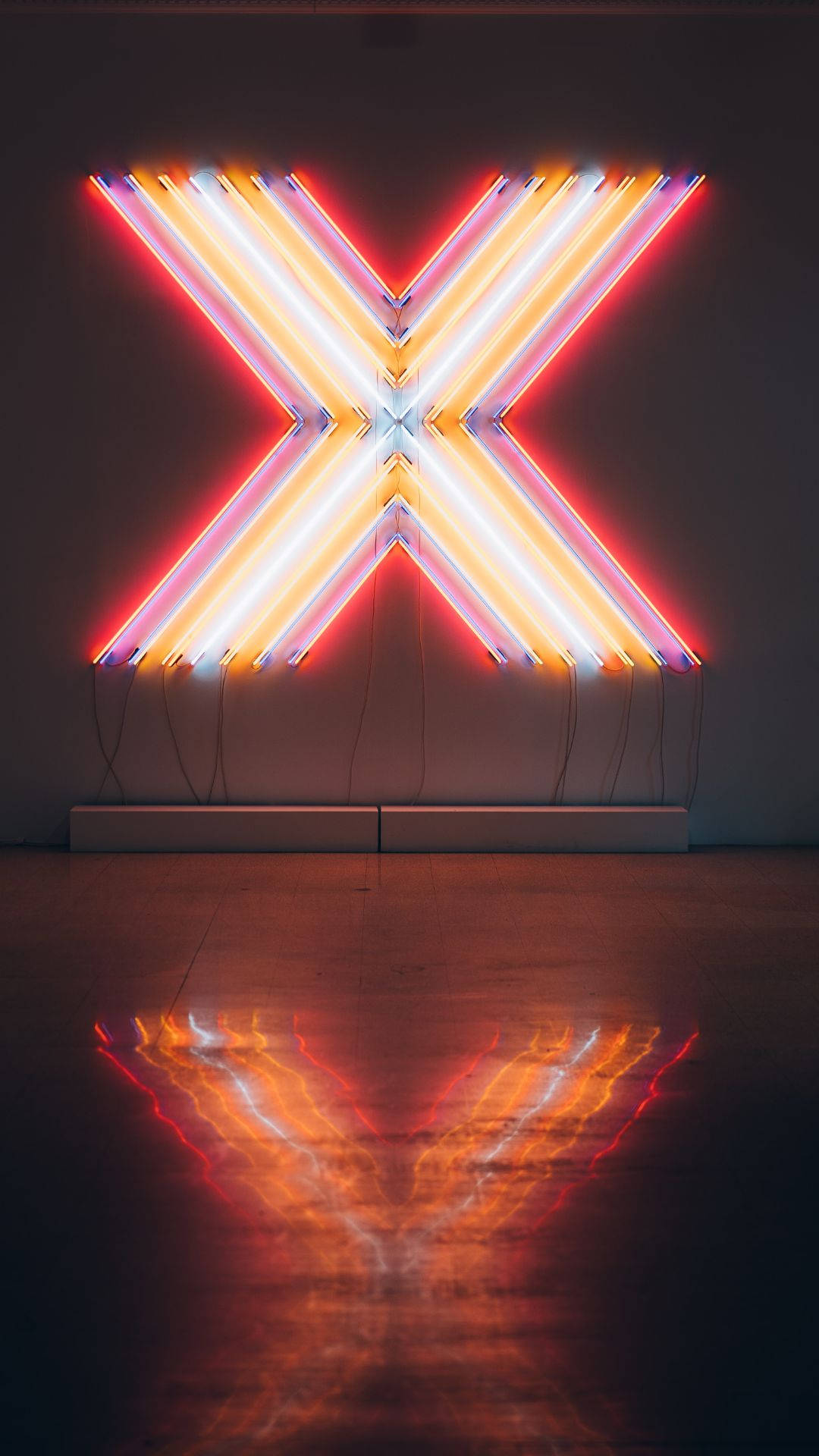 Neon Phone 桌布 壁紙 — 一個發光的霓虹燈X雕塑，以紅、橙、白色在極簡主義畫廊空間的深色拋光地板上投射出鮮明的倒影。