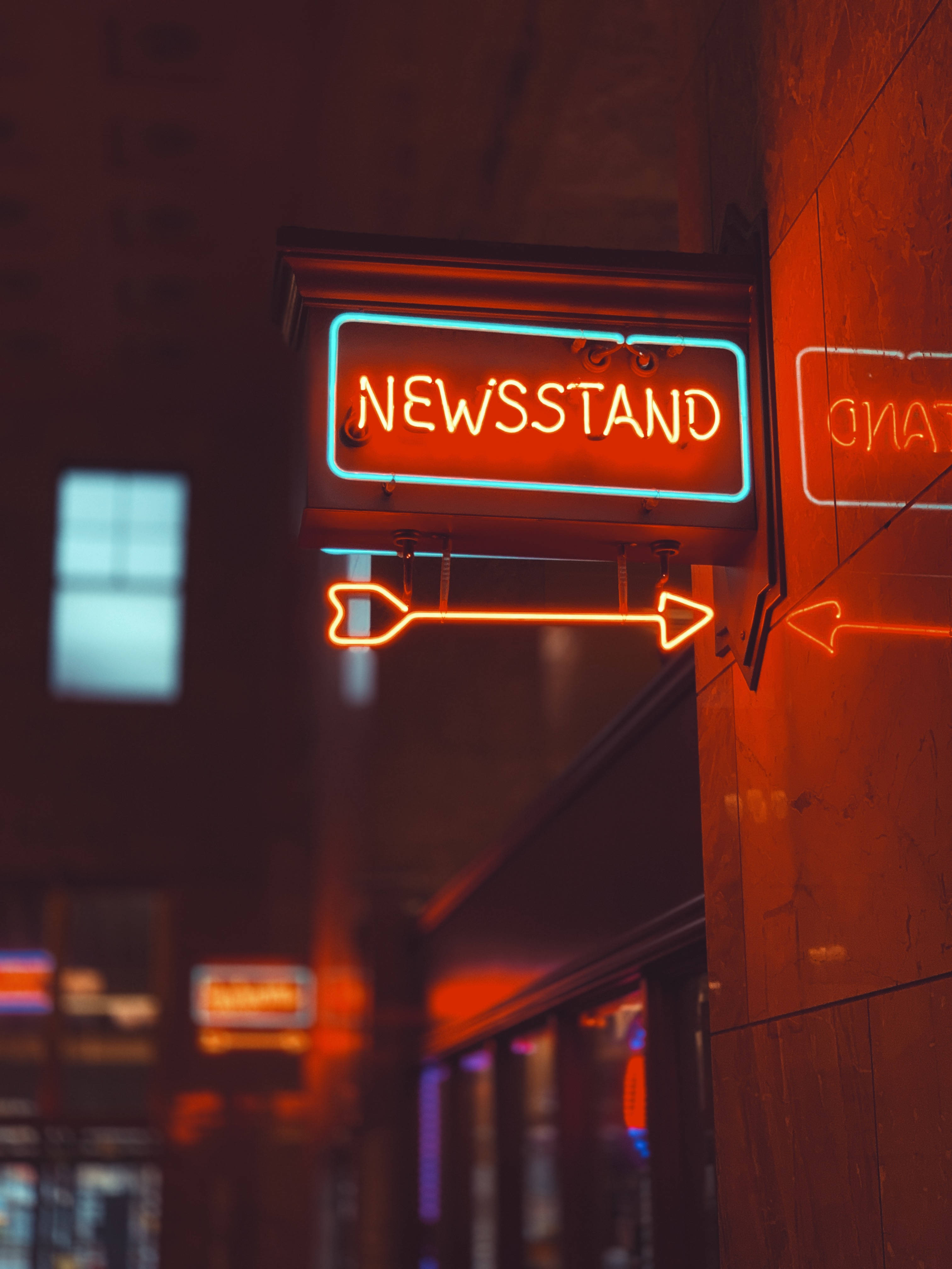 Neon Phone 桌布 壁紙 — 一個發光的霓虹燈招牌，上面寫著newsstand，並有一個箭頭指向右方，位於夜晚黑暗的城市牆上。
