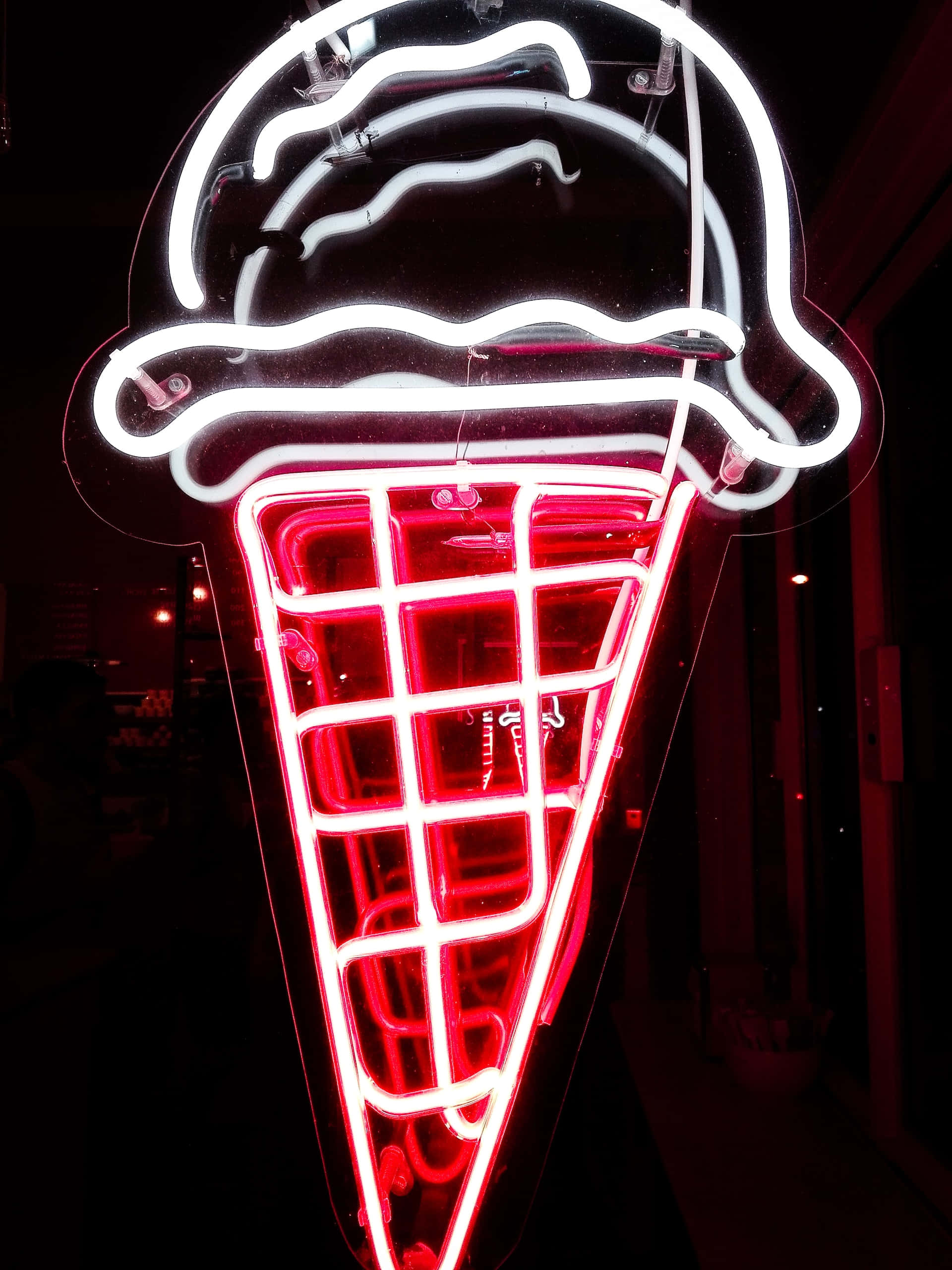Psychedelic Neon Lights 桌布 壁紙 — 一個發光的霓虹燈標誌，形狀像冰淇淋甜筒，帶有白色漩渦和紅色網格圖案，背景為深色。