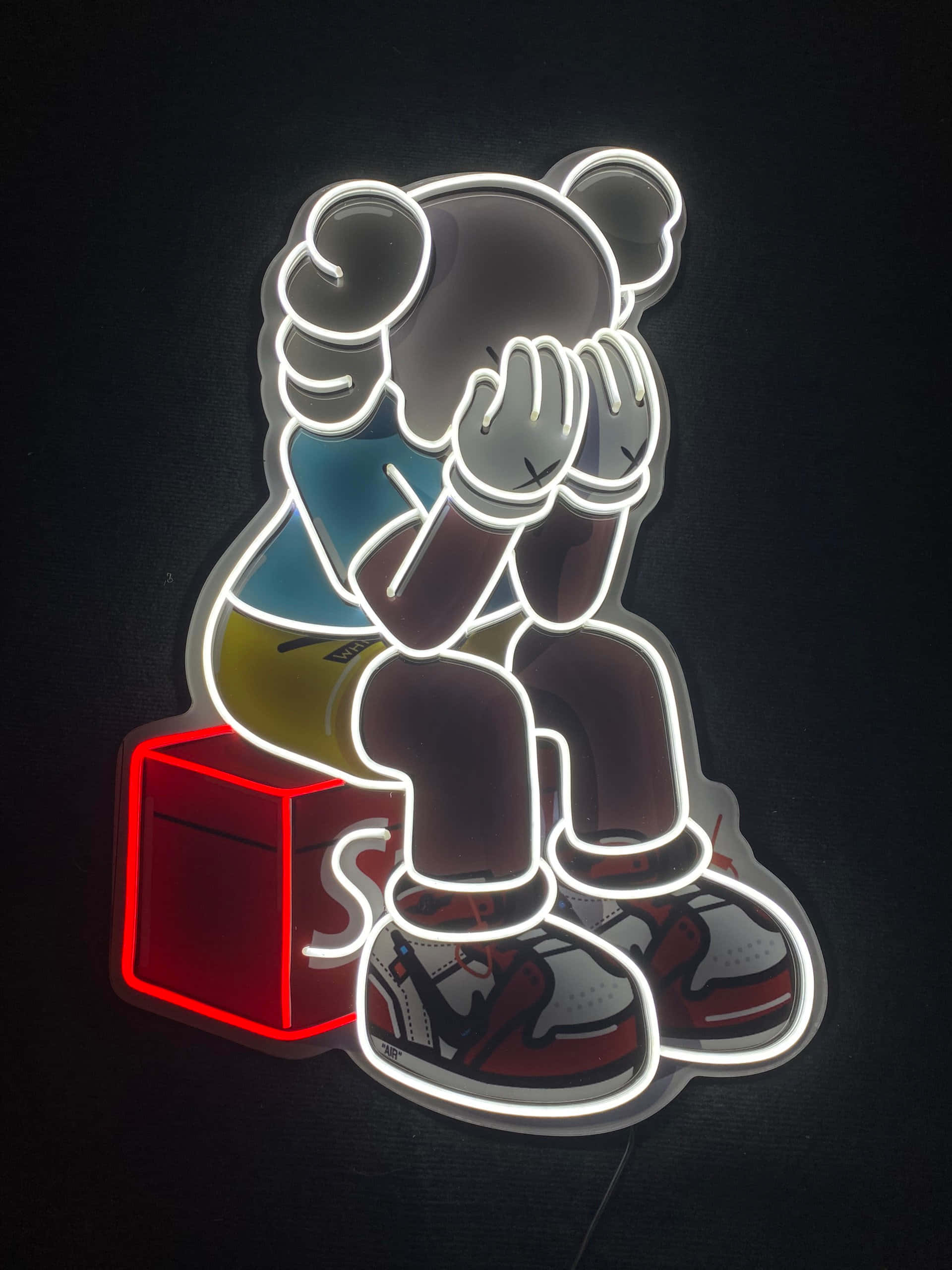 Kaws X Supreme 桌布 壁紙 — 一個發光的霓虹燈標誌，描繪一隻卡通熊坐在紅色立方體上，雙手遮臉，背景為深色。