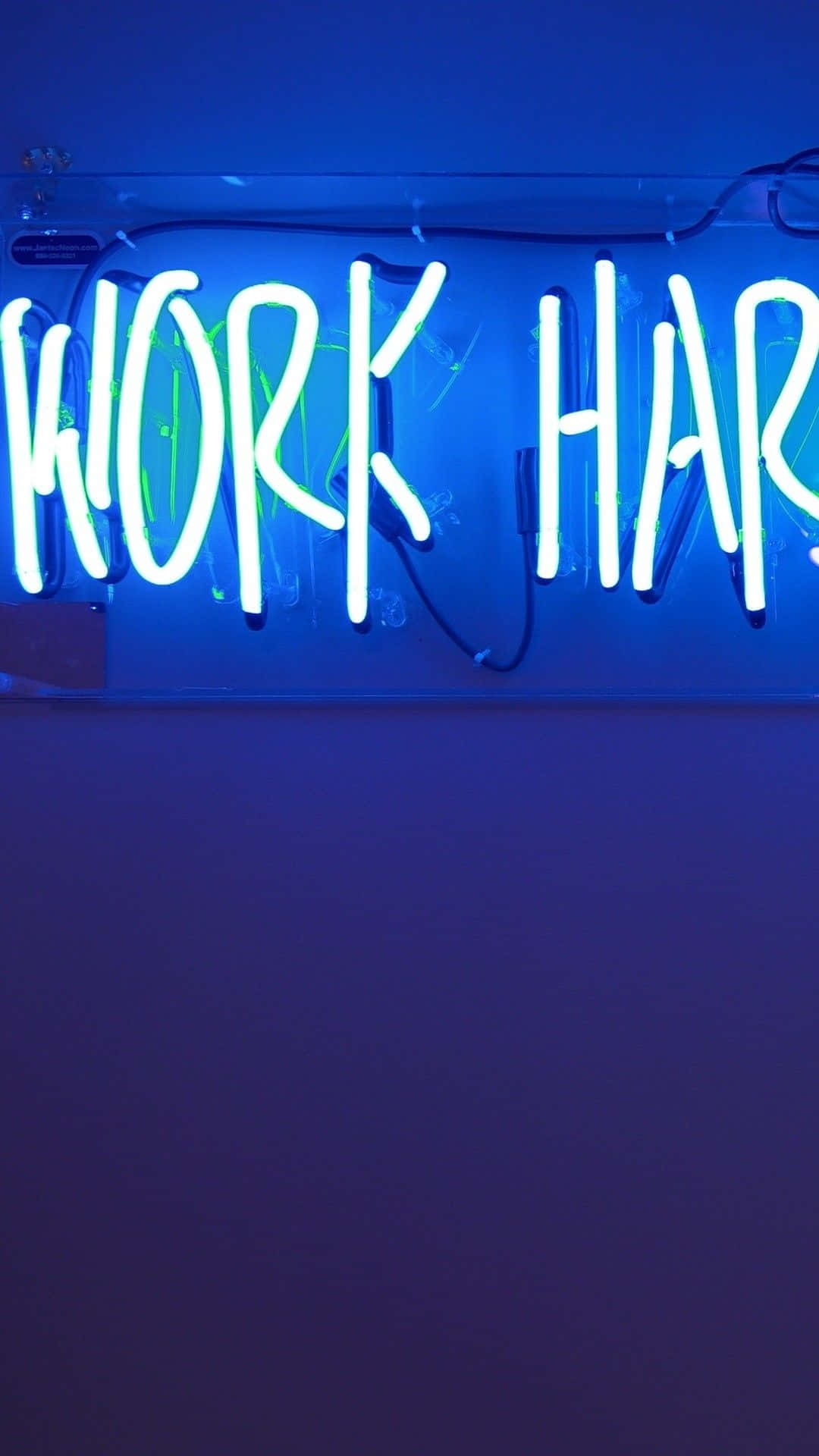iPhone Neon 桌布 壁紙 — 一個發光的霓虹燈牌寫著 work hard，背景是深藍色牆壁，有可見的電線和微弱的綠色輪廓。
