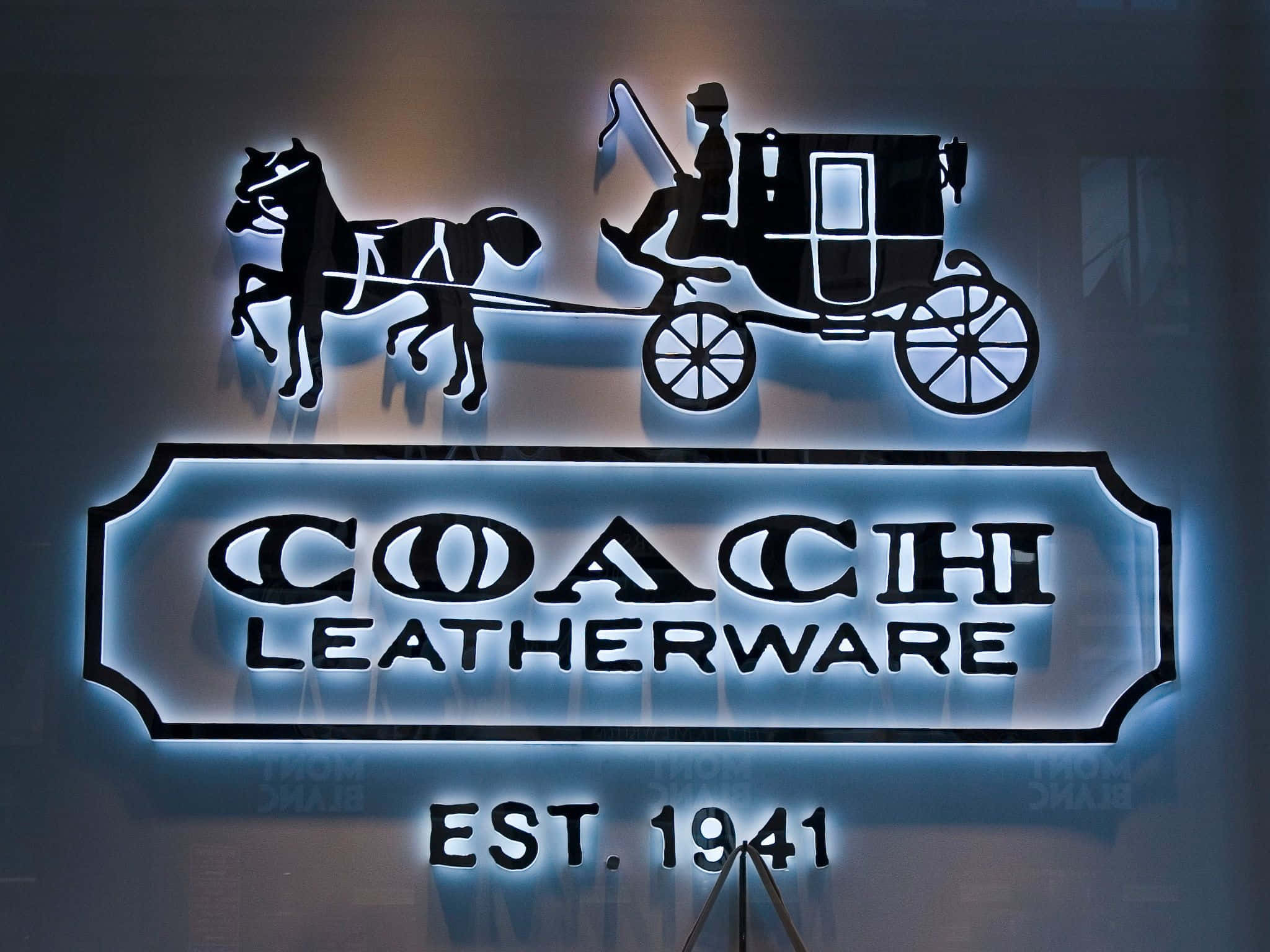 Coach 桌布 壁紙 — 一個發光的霓虹燈牌顯示一輛馬車和車夫的剪影，上方是品牌名稱 coach leatherware est 1941。