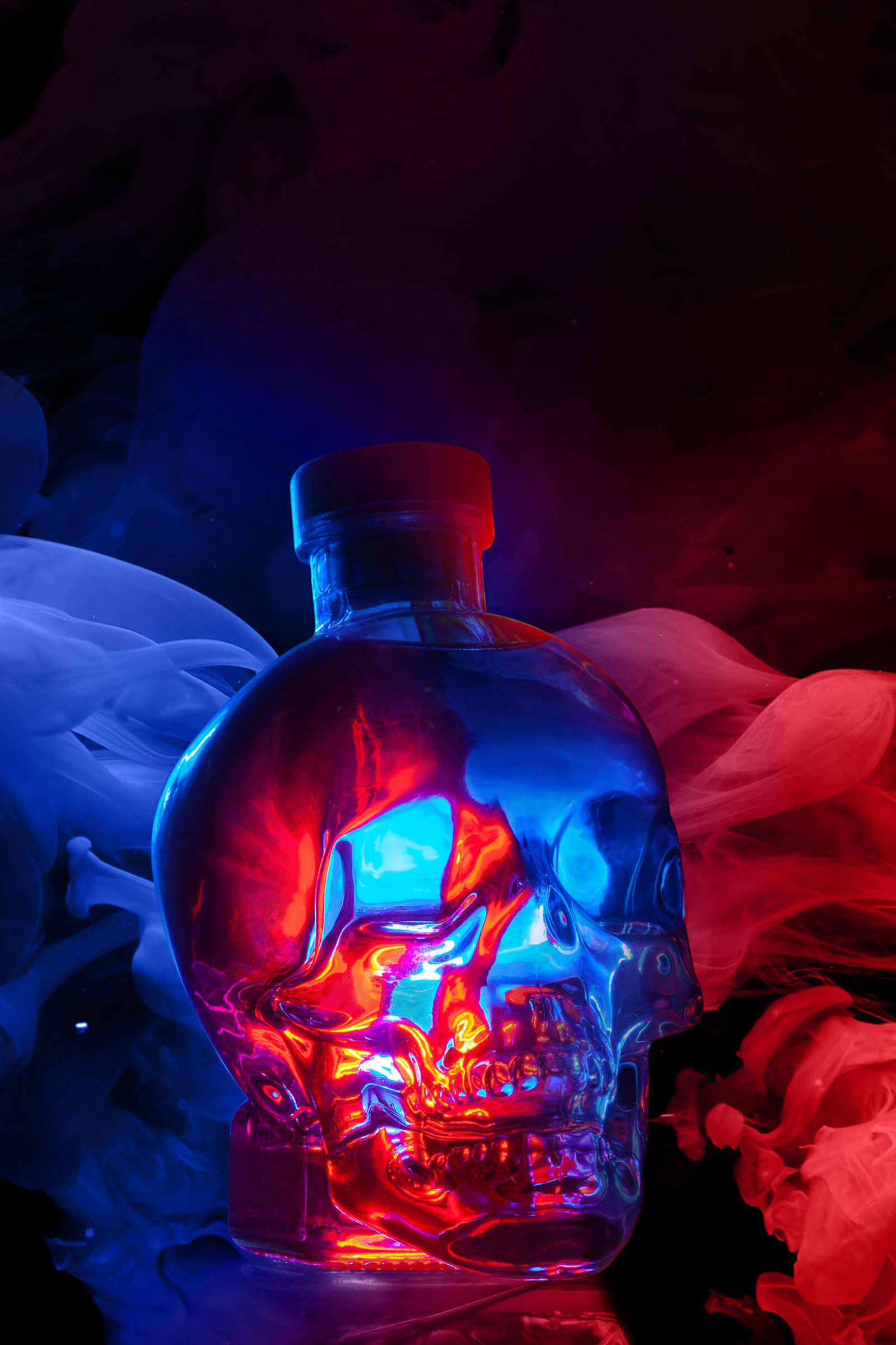 Drink 桌布 壁紙 — 一個發光的骷髏形瓶子，被紅色和藍色的燈光照亮，周圍環繞著旋轉的煙霧。