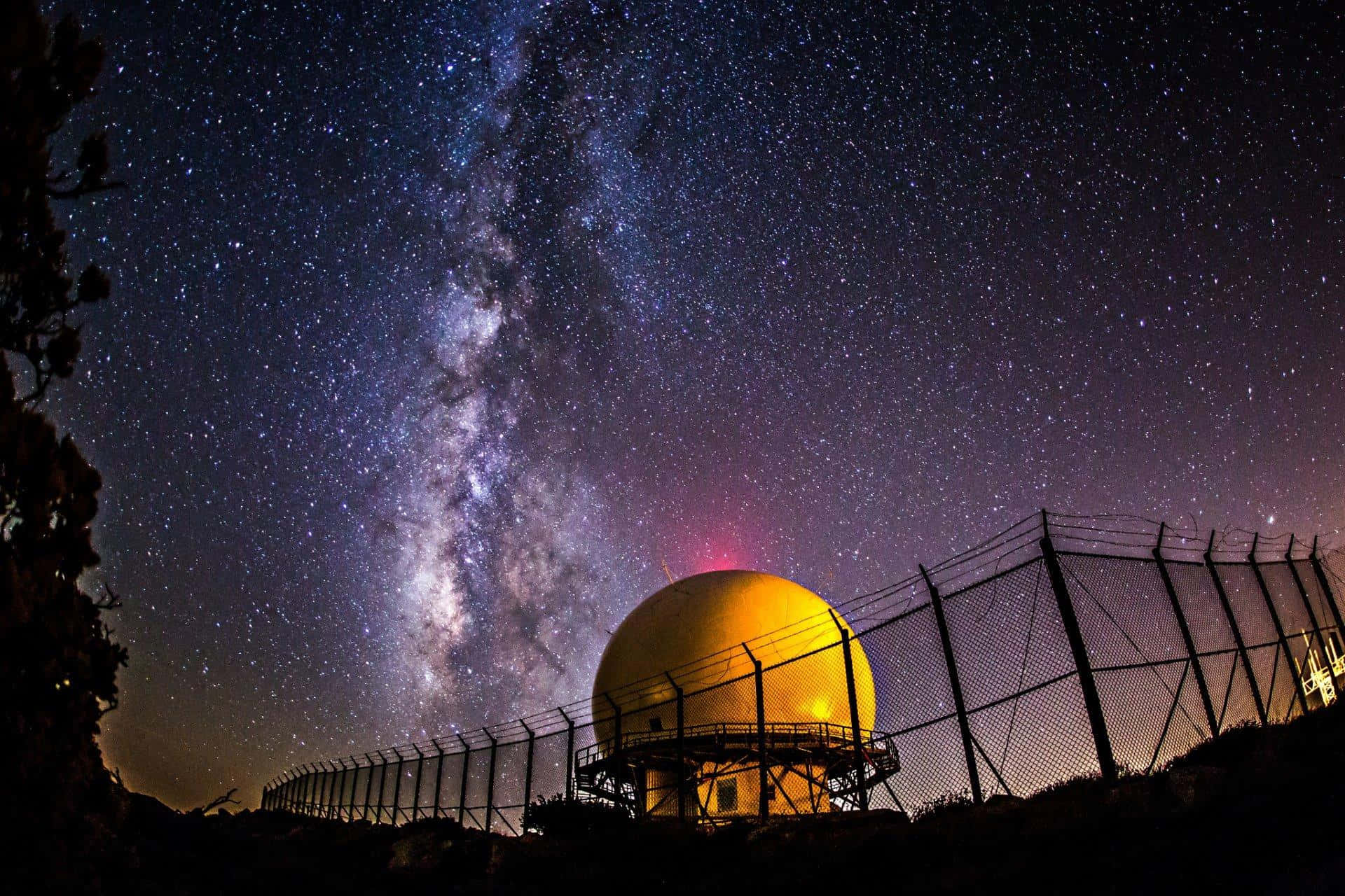 Space Observation 桌布 壁紙 — 一個發光的黃色雷達圓頂矗立在令人驚嘆的星空下，銀河在其上方拱起。