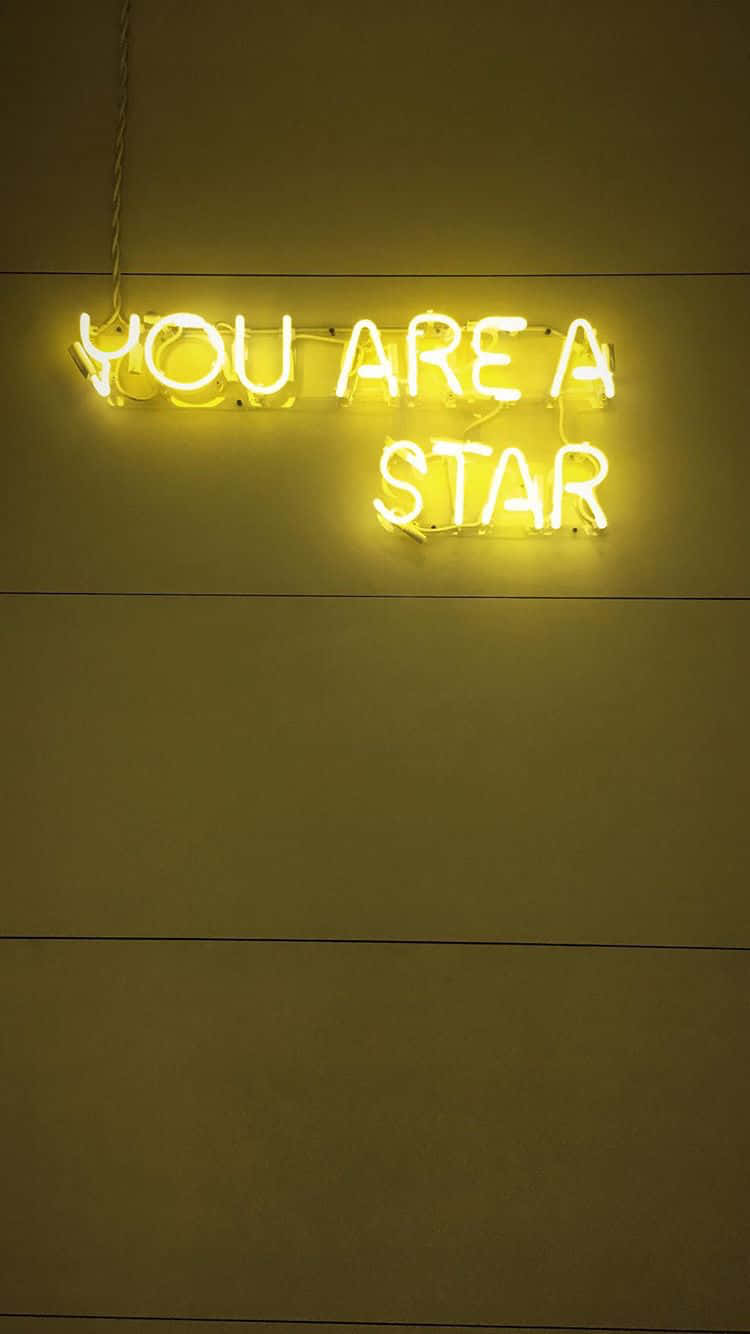 桌布 壁紙 — 一個發光的黃色霓虹燈牌，上面寫著「YOU ARE A STAR」，掛在一個光線昏暗的房間裡的純米色牆上。