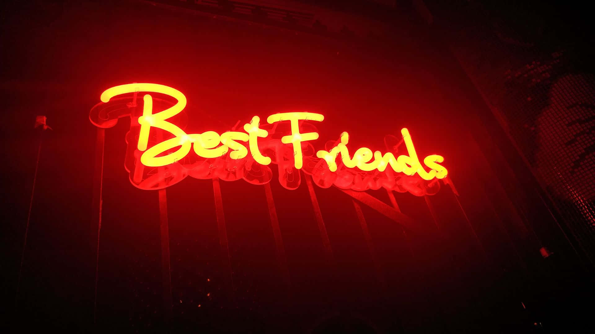 摯友 桌布 壁紙 — 一個發光的黃色霓虹燈牌，上面寫著 'Best Friends'，在黑暗背景下投射出溫暖的紅色光芒。