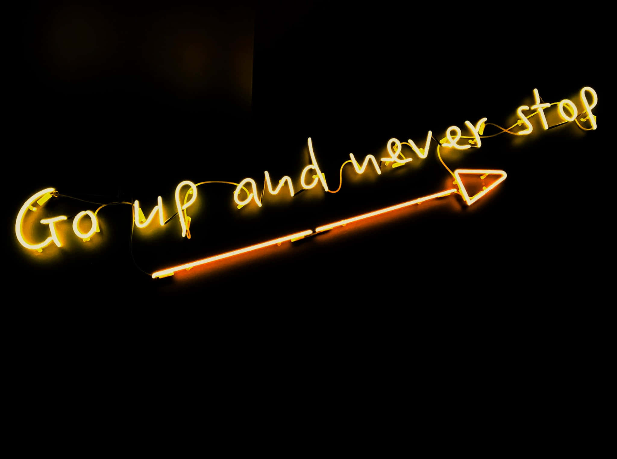 桌布 壁紙 — 一個發光的黃色霓虹燈牌，上面寫著「Go up and never stop」，並有一個向上指的箭頭，背景為黑色。