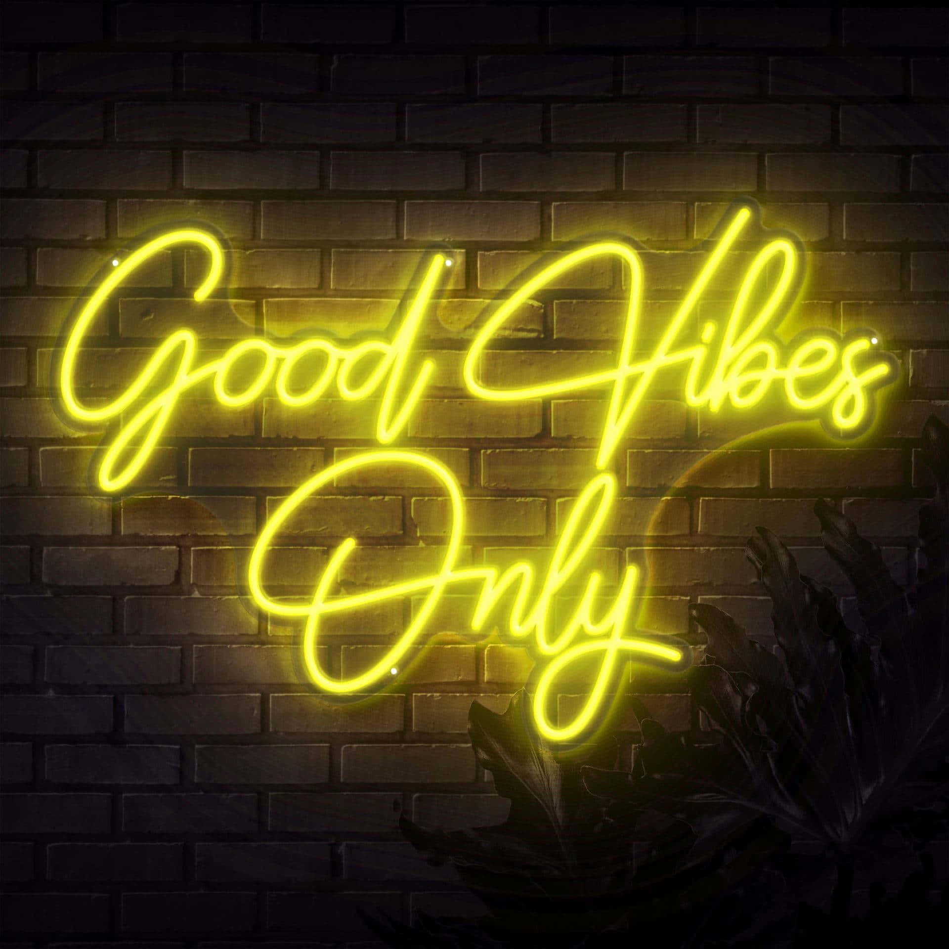 桌布 壁紙 — 一個發光的黃色霓虹燈牌，上面寫著「Good Vibes Only」，照亮了深色磚牆，下方有茂密的綠色植物。