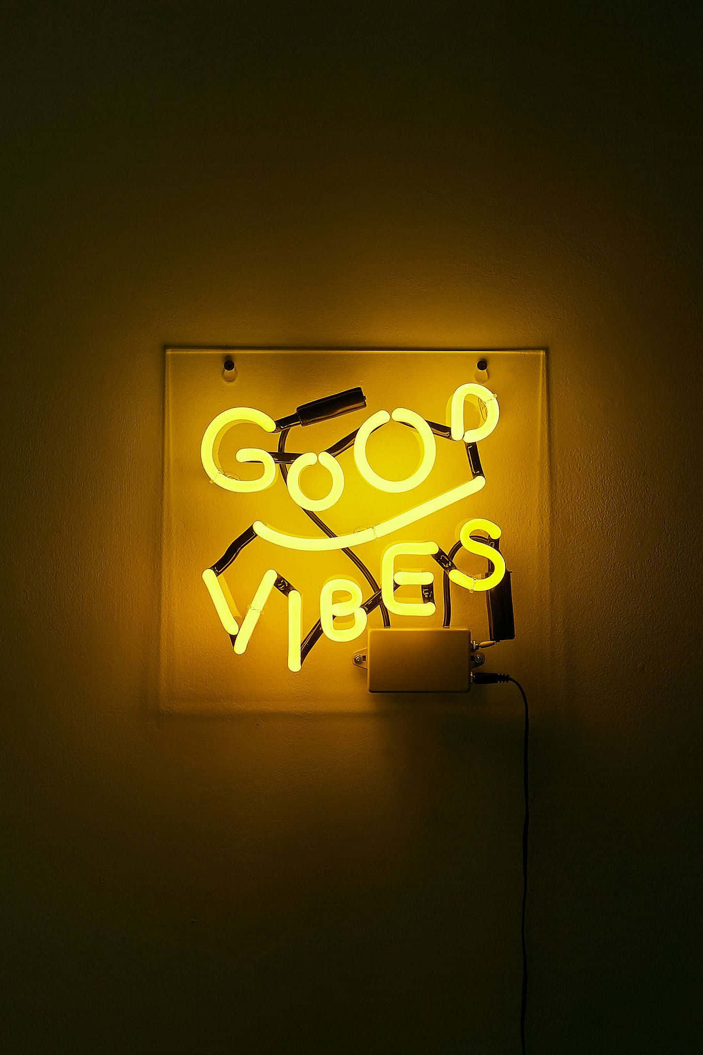 Led Light 桌布 壁紙 — 一個發光的黃色霓虹燈牌，上面寫著「GOOD VIBES」和一個笑臉，在黑暗的牆壁上投射出溫暖的光芒。