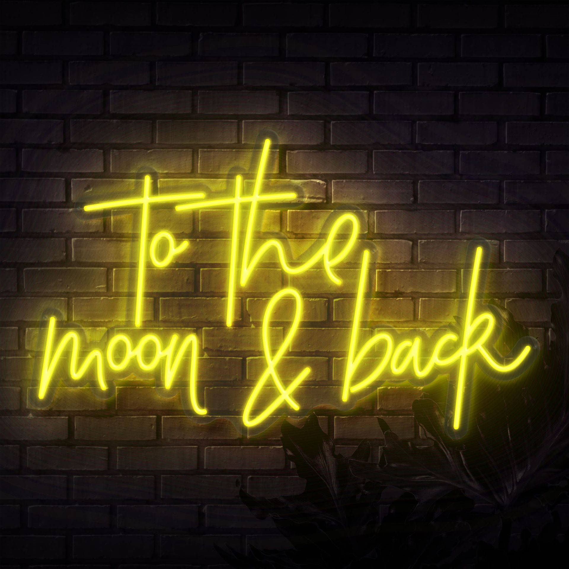 螢光黃 桌布 壁紙 — 一個發光的黃色霓虹燈牌，上面寫著「to the moon & back」，照亮了深色磚牆和下方的葉子剪影。