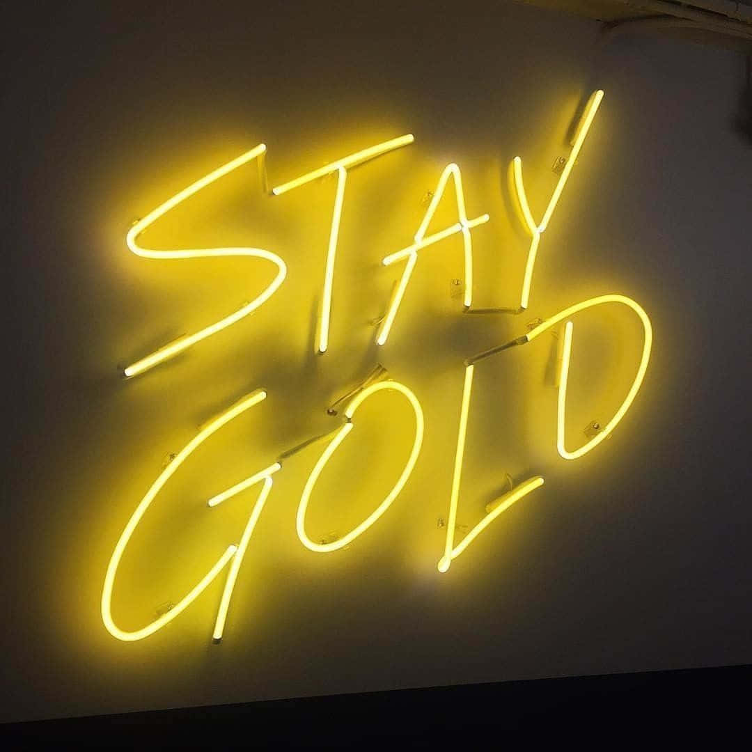 霓虹美學 桌布 壁紙 — 一個發光的黃色霓虹燈牌，以草書寫著「STAY GOLD」，背景是暗色牆壁。