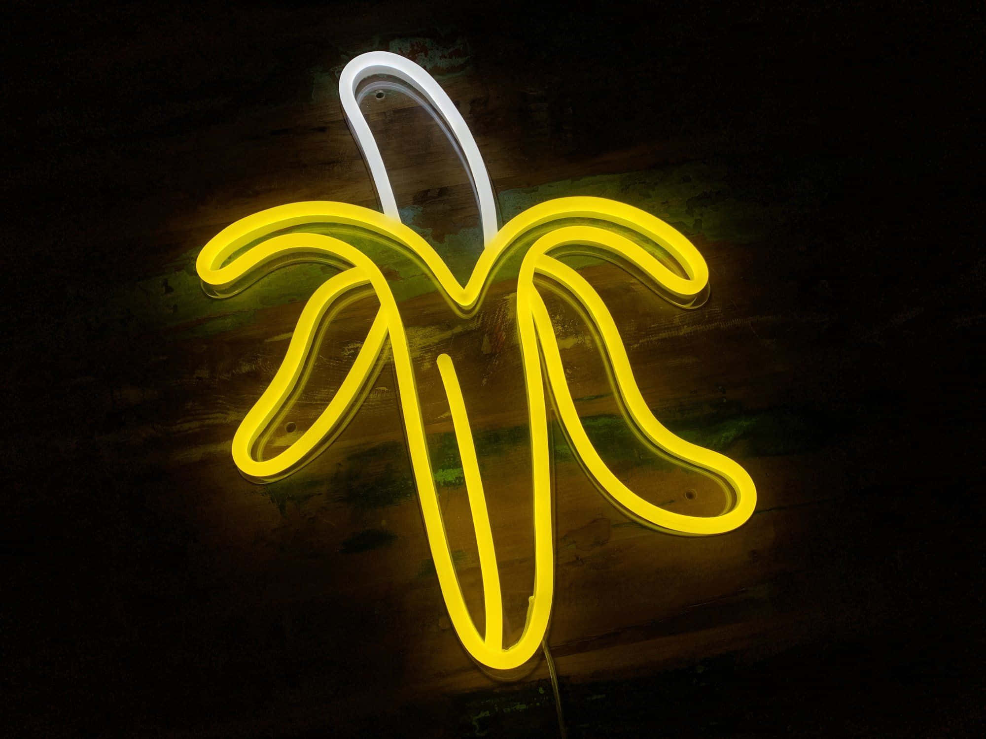 Neon Lights Aesthetic 桌布 壁紙 — 一個發光的黃色霓虹燈牌，形狀像香蕉，帶有白色莖，背景是深色紋理牆壁。
