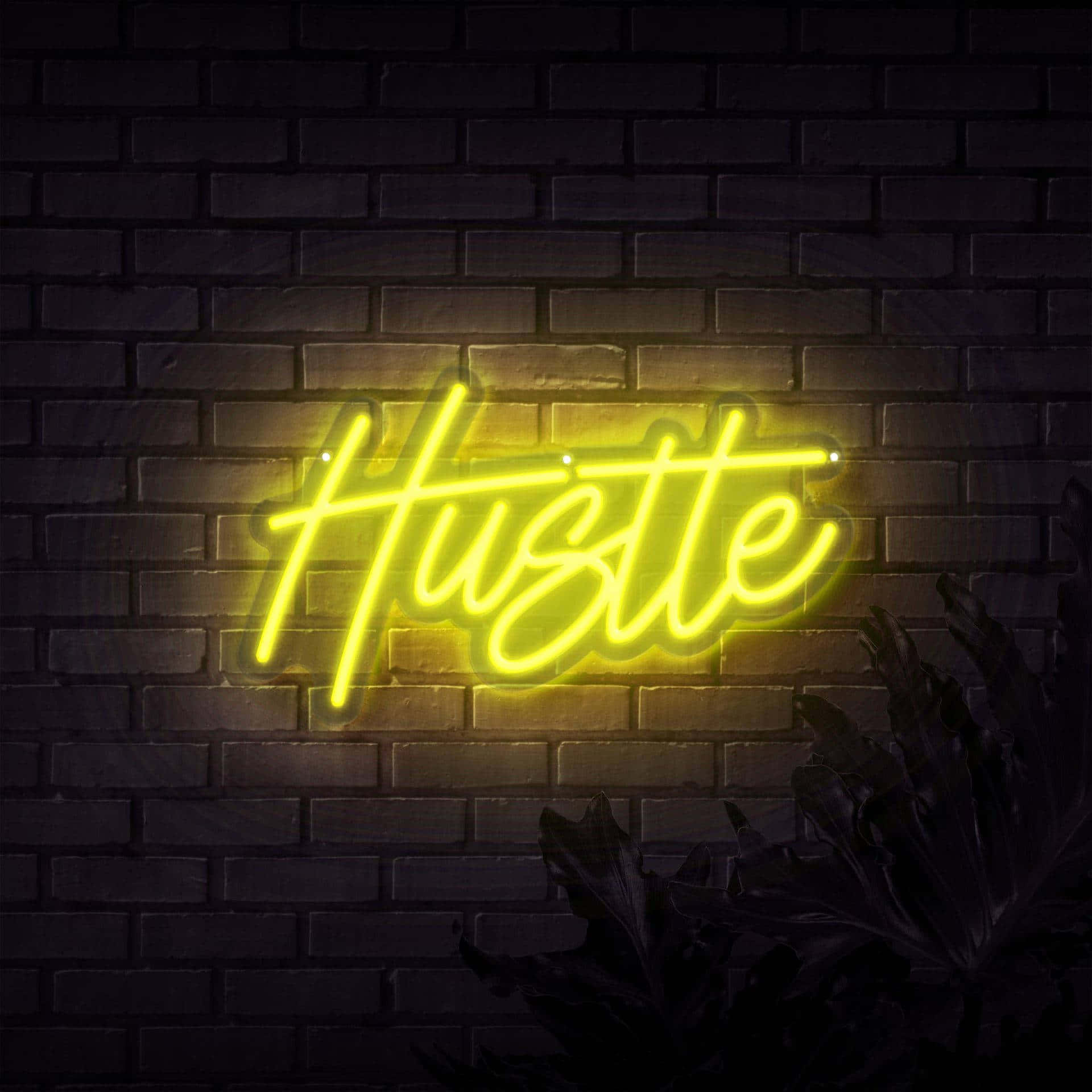桌布 壁紙 — 一個發光的黃色霓虹燈牌，拼出「Hustle」，照亮了深色磚牆和下方剪影般的葉子。