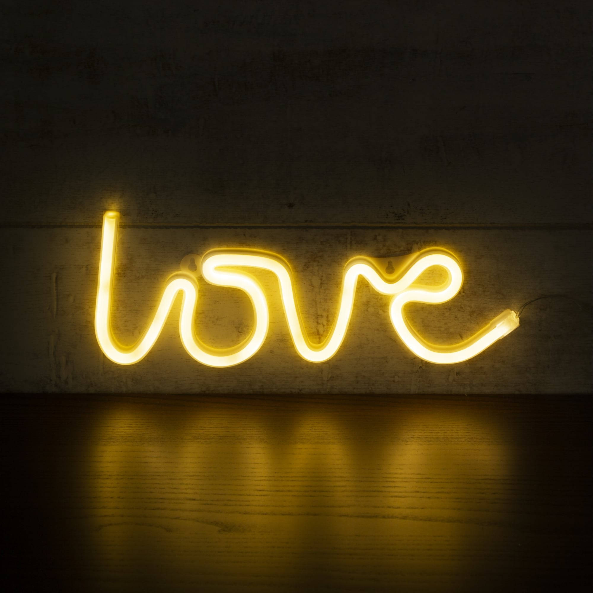 螢光黃 桌布 壁紙 — 一個發光的黃色霓虹燈牌拼出love，在深色紋理牆壁的背景下，在木地板上投射出溫暖的倒影。