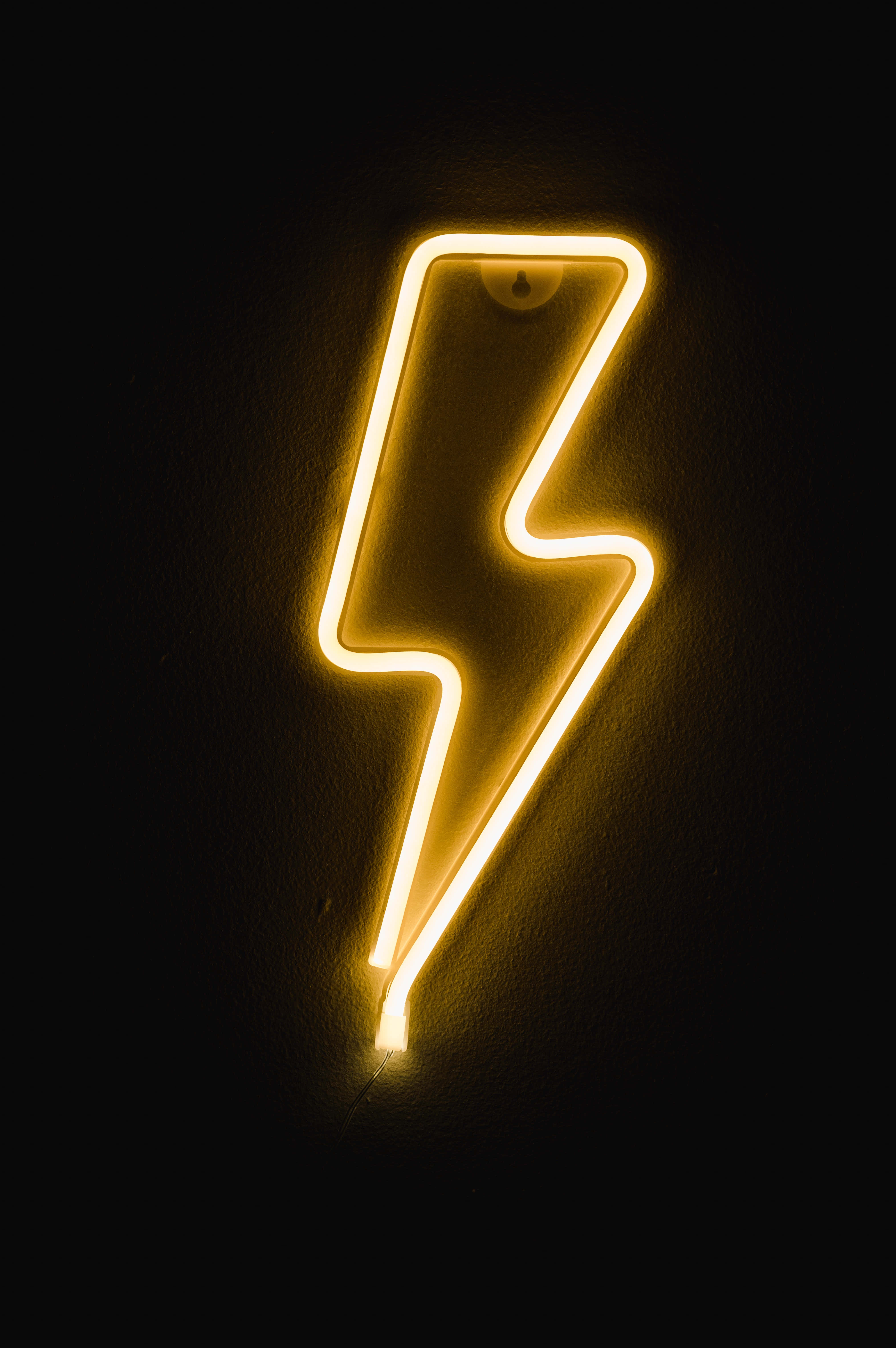 Lightning Bolt 桌布 壁紙 — 一個發光的黃色霓虹閃電標誌，在深色紋理牆壁上投射出溫暖的光芒。